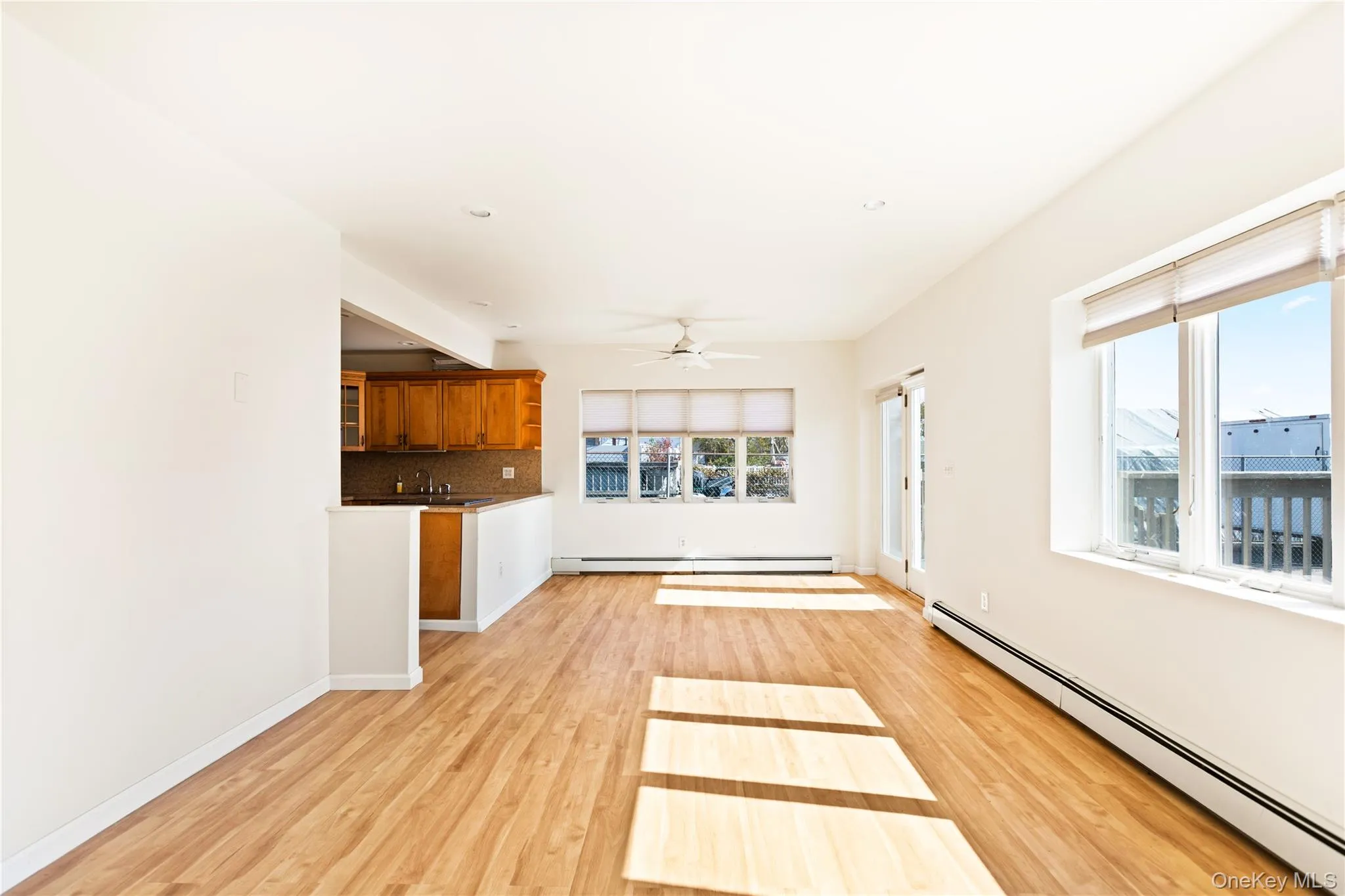 Unfurnished living room featuring a baseboard heating unit, light wood-type flooring, and a ceiling fan Unfurnished living room featuring a baseboard heating unit, light wood-type flooring, and a ceiling fan