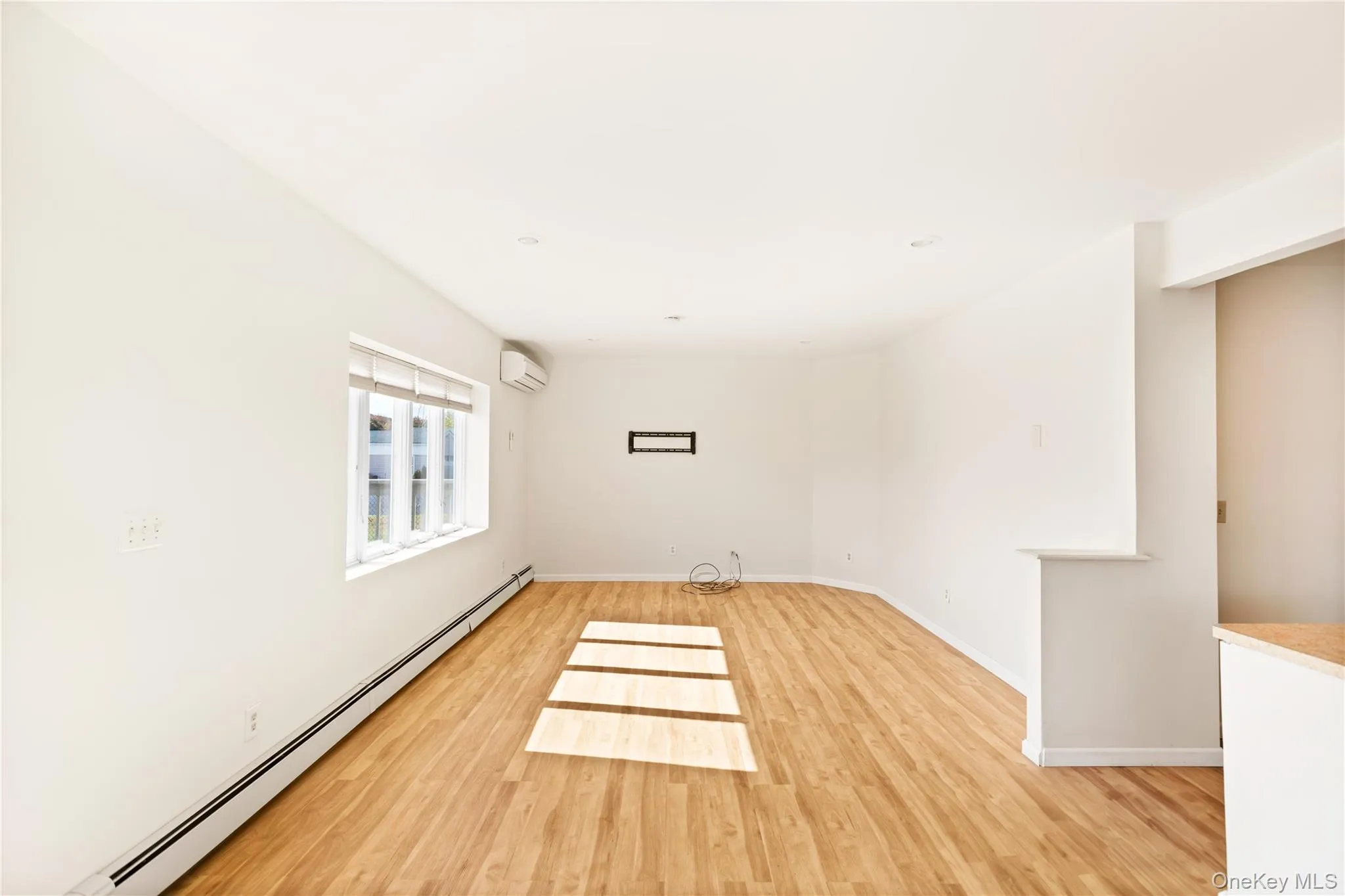 Living room featuring a baseboard heating unit, light wood-style flooring, and a wall mounted air conditioner Living room featuring a baseboard heating unit, light wood-style flooring, and a wall mounted air conditioner