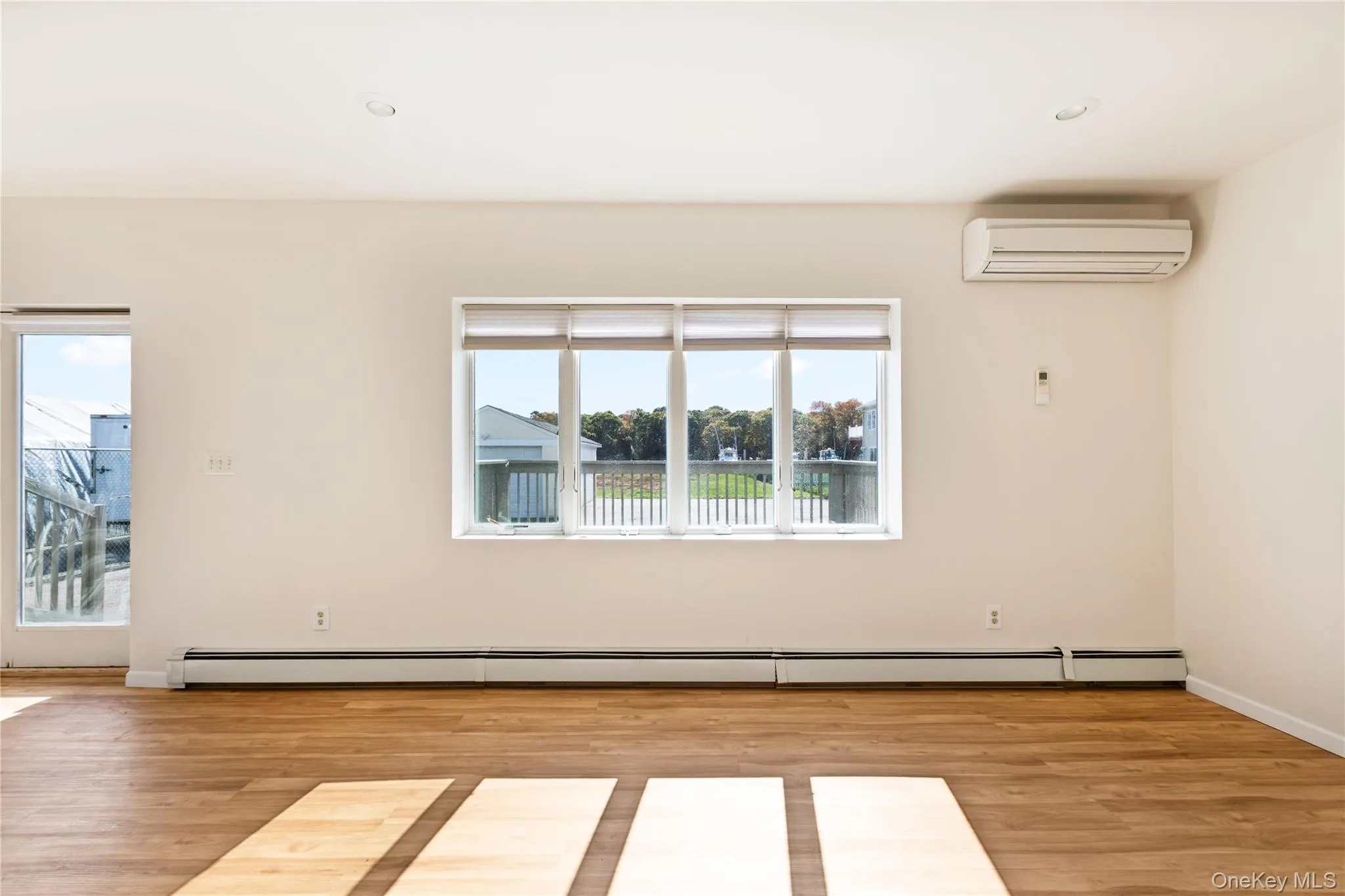 Living room with light wood-style floors, a wall mounted air conditioner, and a baseboard heating unit Living room with light wood-style floors, a wall mounted air conditioner, and a baseboard heating unit