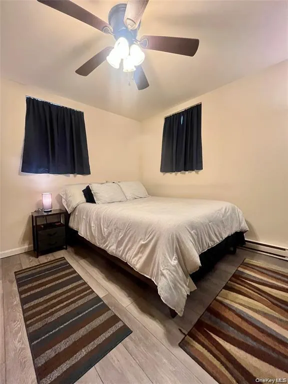 Bedroom featuring a ceiling fan, baseboard heating, and light wood-style floors Bedroom featuring a ceiling fan, baseboard heating, and light wood-style floors