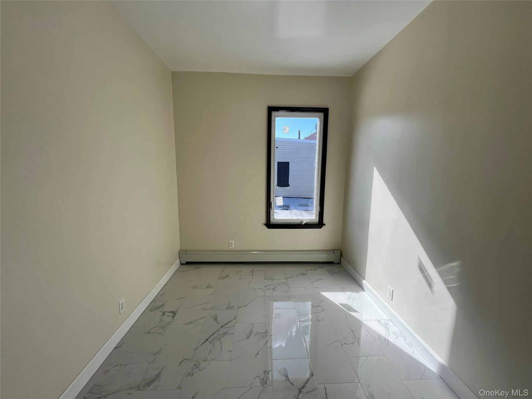 Unfurnished room with light marble finish flooring and baseboard heating Unfurnished room with light marble finish flooring and baseboard heating