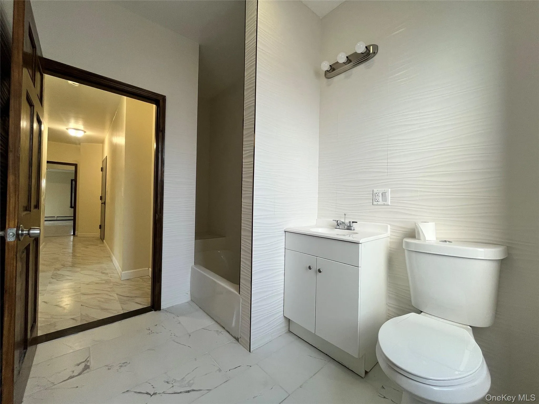 Bathroom featuring light marble finish flooring, vanity, and a bath Bathroom featuring light marble finish flooring, vanity, and a bath