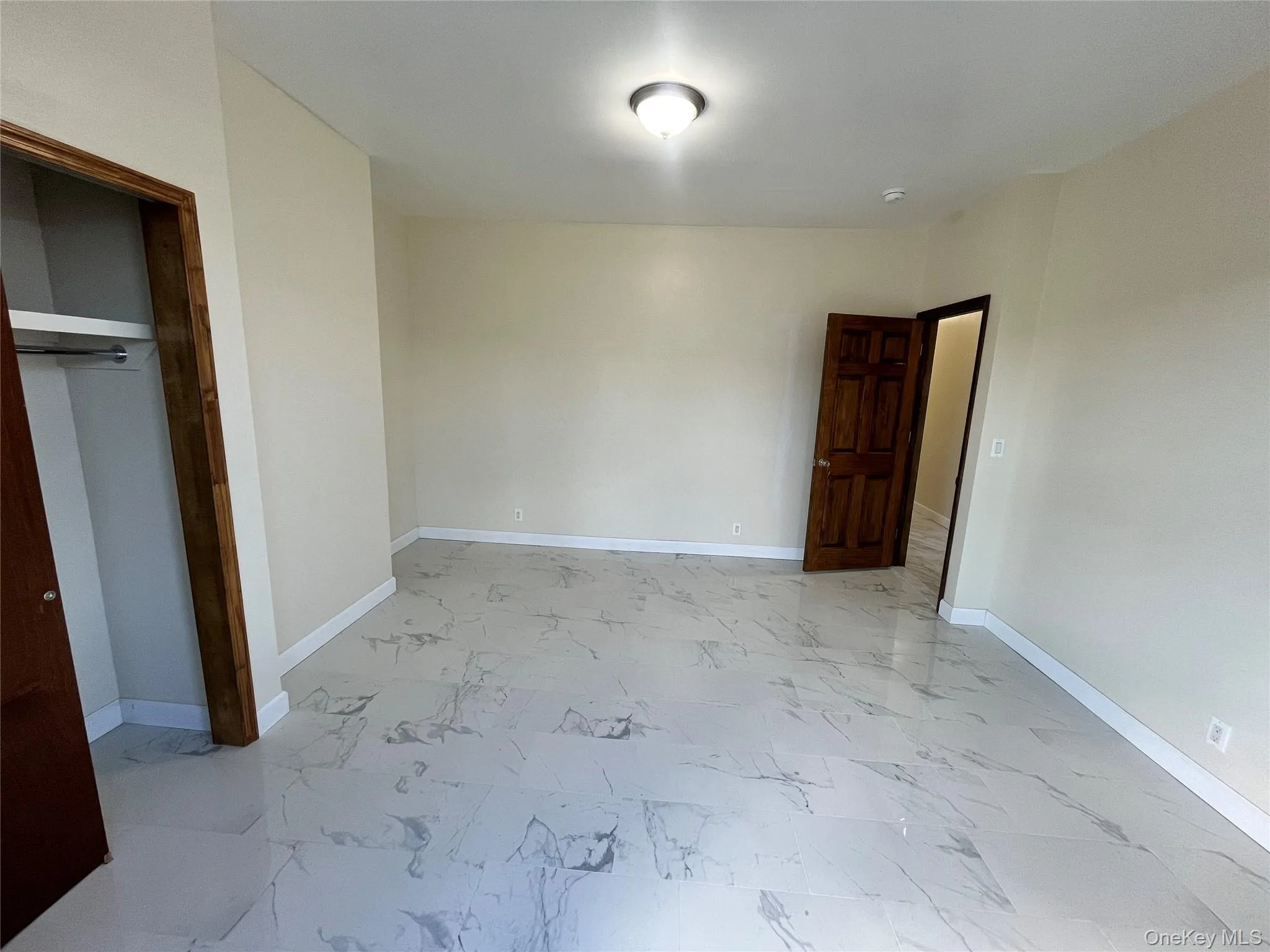 Unfurnished bedroom featuring light marble finish flooring and a closet Unfurnished bedroom featuring light marble finish flooring and a closet