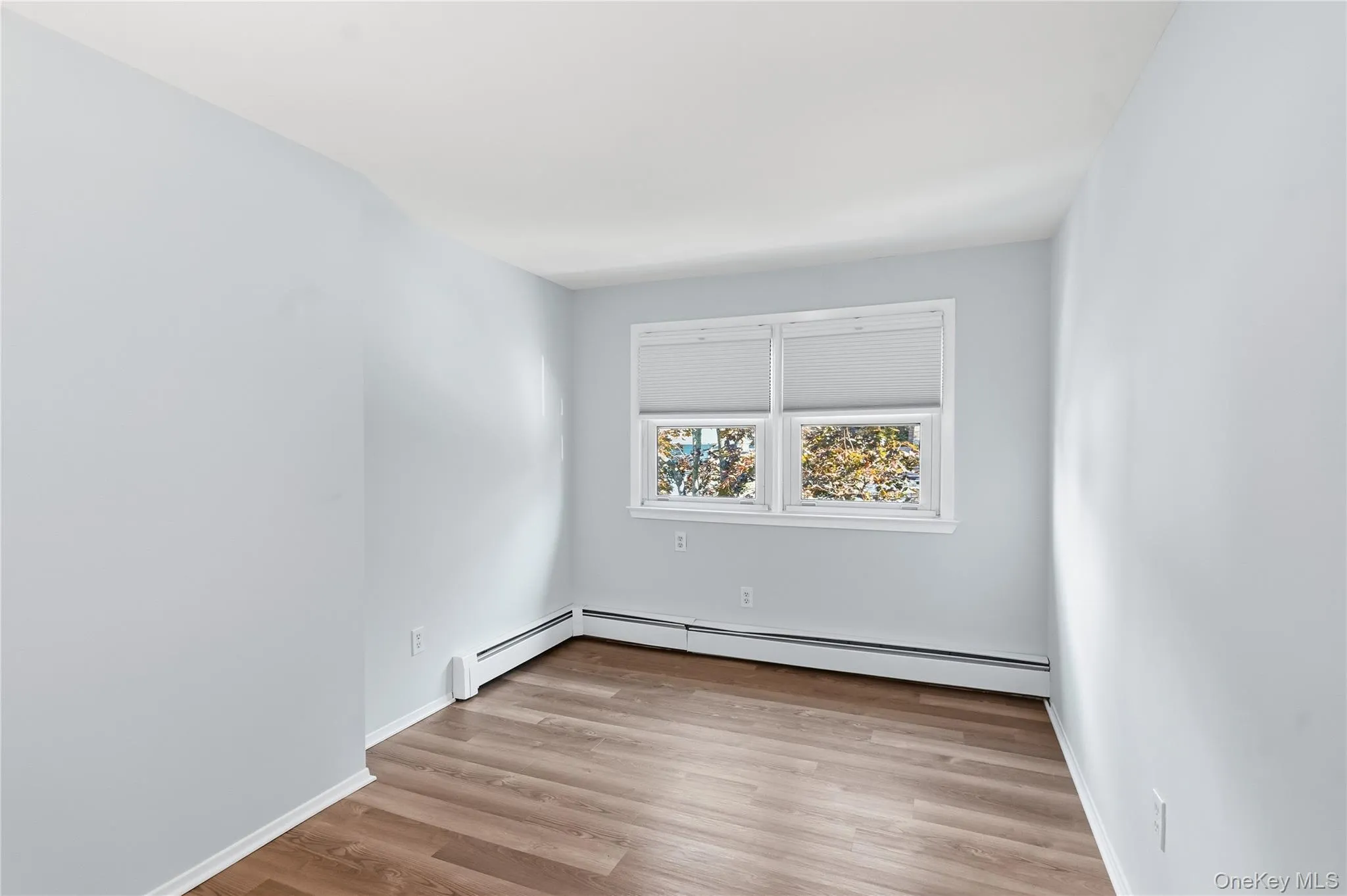 Unfurnished room featuring light wood-style flooring and baseboard heating Unfurnished room featuring light wood-style flooring and baseboard heating