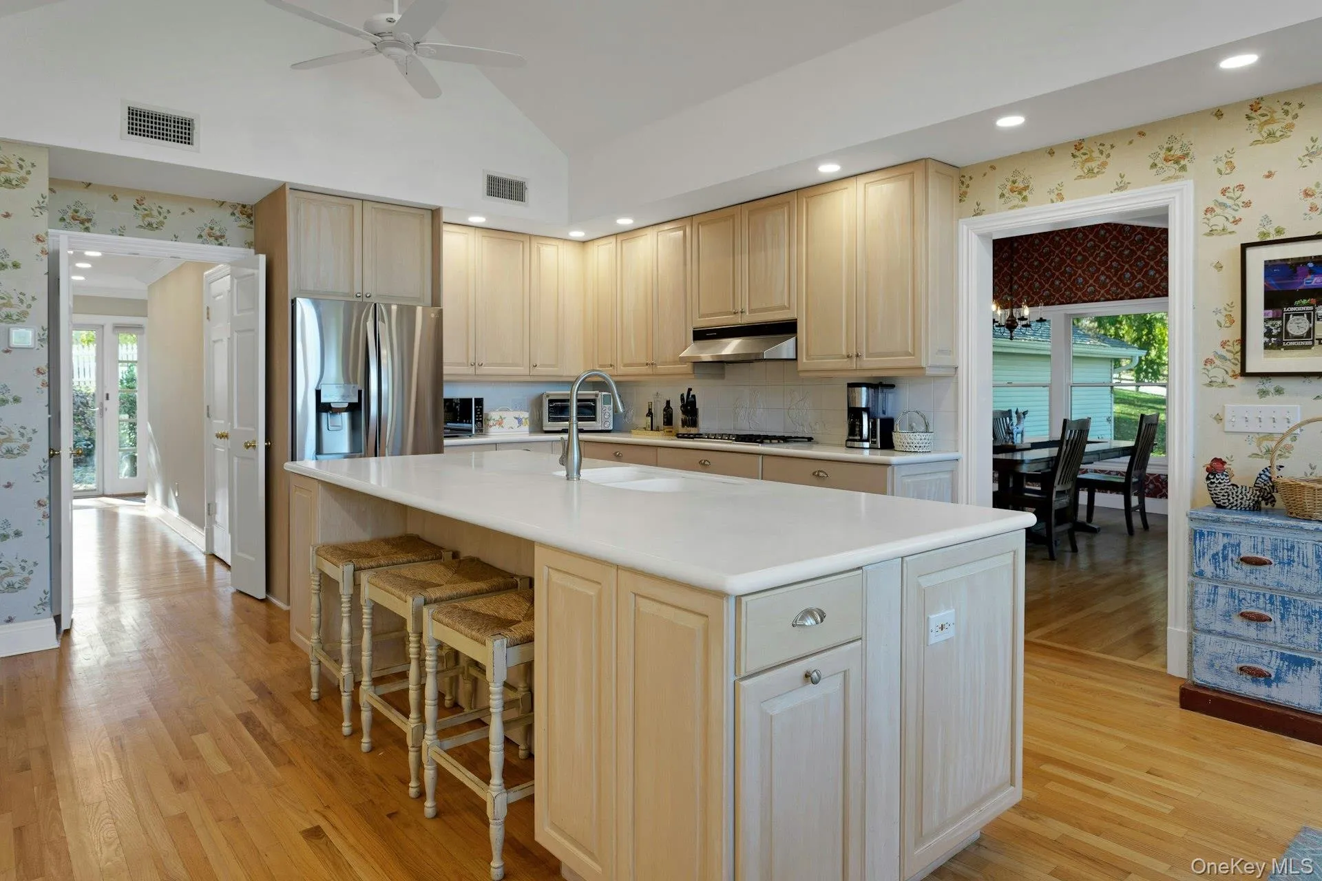 Kitchen with wallpapered walls, stainless steel fridge with ice dispenser, light wood finished floors, a center island with sink, and a breakfast bar area Kitchen with wallpapered walls, stainless steel fridge with ice dispenser, light wood finished floors, a center island with sink, and a breakfast bar area