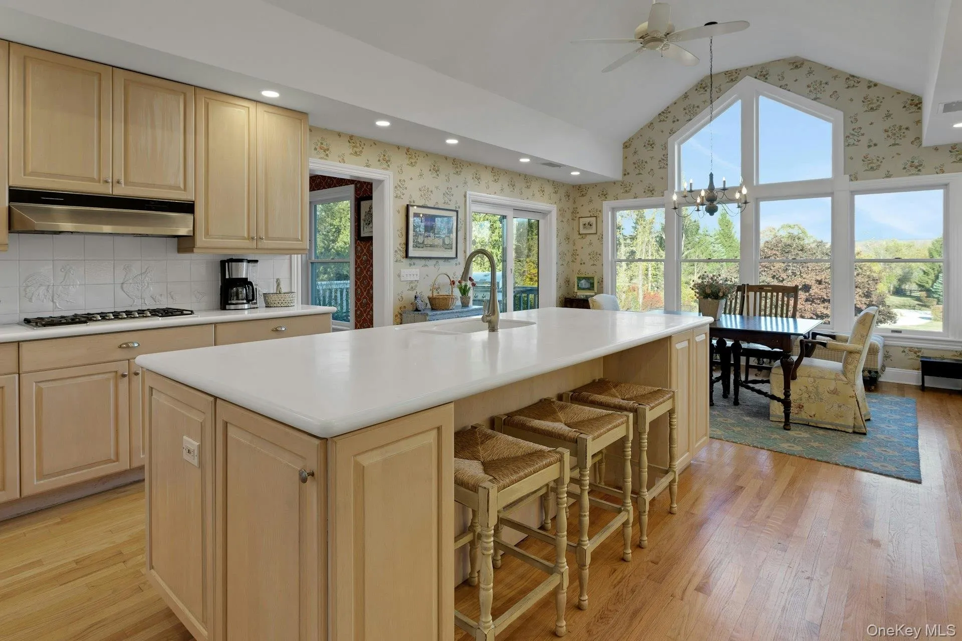 Kitchen featuring wallpapered walls, light brown cabinetry, light wood-style floors, a chandelier, and lofted ceiling Kitchen featuring wallpapered walls, light brown cabinetry, light wood-style floors, a chandelier, and lofted ceiling