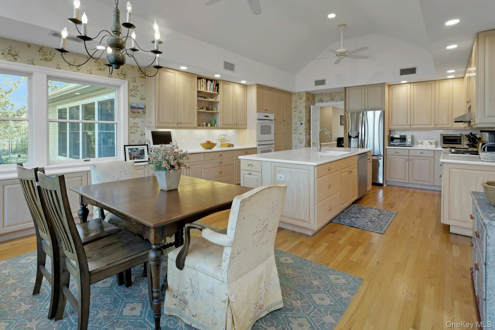 Dining area with a chandelier, lofted ceiling, light wood-style floors, wallpapered walls, and a ceiling fan Dining area with a chandelier, lofted ceiling, light wood-style floors, wallpapered walls, and a ceiling fan