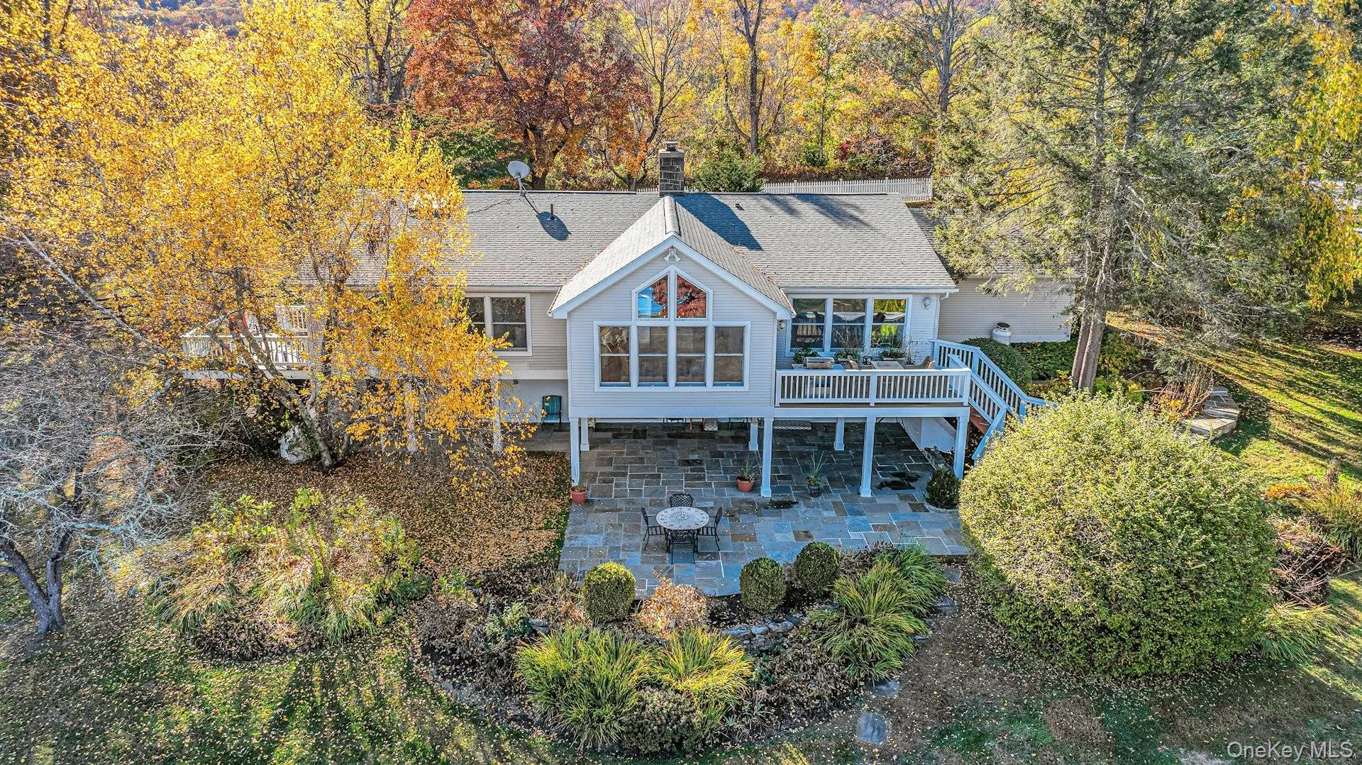 Rear view of property with a chimney, a patio area, a wooden deck, a shingled roof, and stairway Rear view of property with a chimney, a patio area, a wooden deck, a shingled roof, and stairway