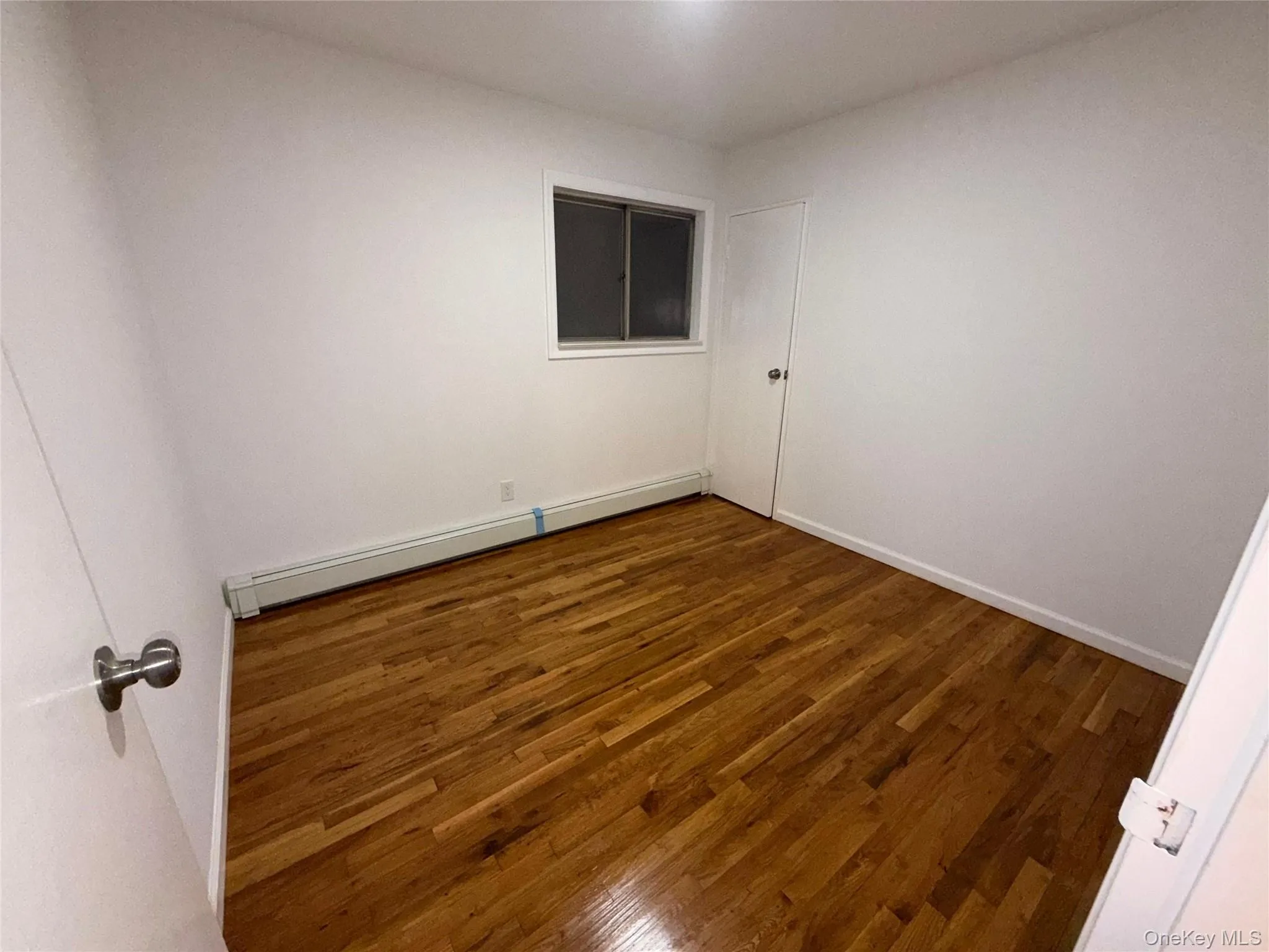 Empty room with wood finished floors and baseboard heating Empty room with wood finished floors and baseboard heating
