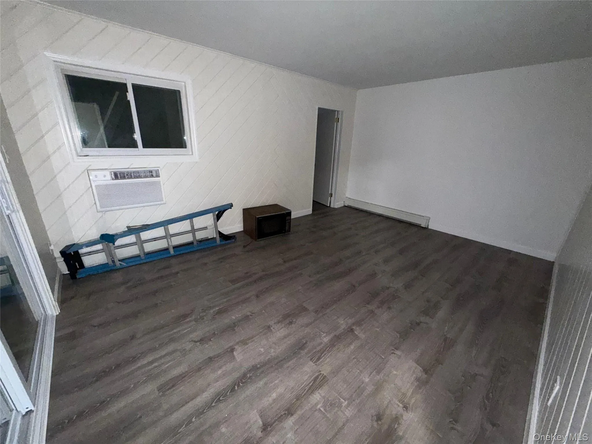 Empty room with dark wood-type flooring, a baseboard heating unit, and baseboard heating Empty room with dark wood-type flooring, a baseboard heating unit, and baseboard heating