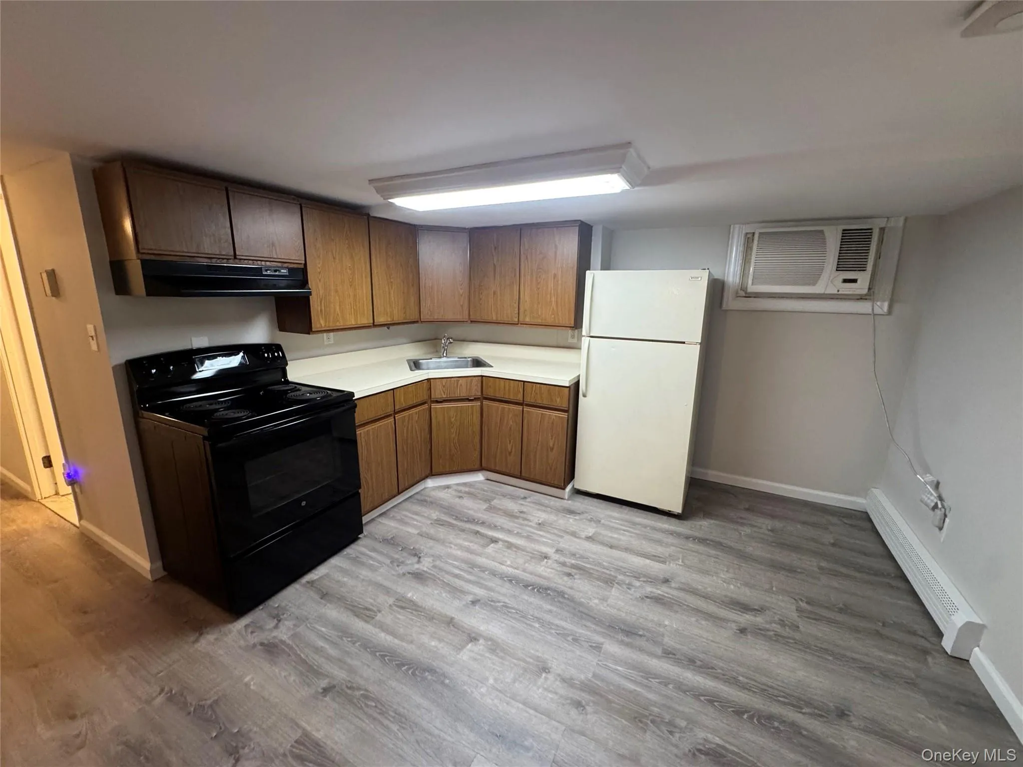 Kitchen with light countertops, black electric range, freestanding refrigerator, a baseboard radiator, and light wood finished floors Kitchen with light countertops, black electric range, freestanding refrigerator, a baseboard radiator, and light wood finished floors