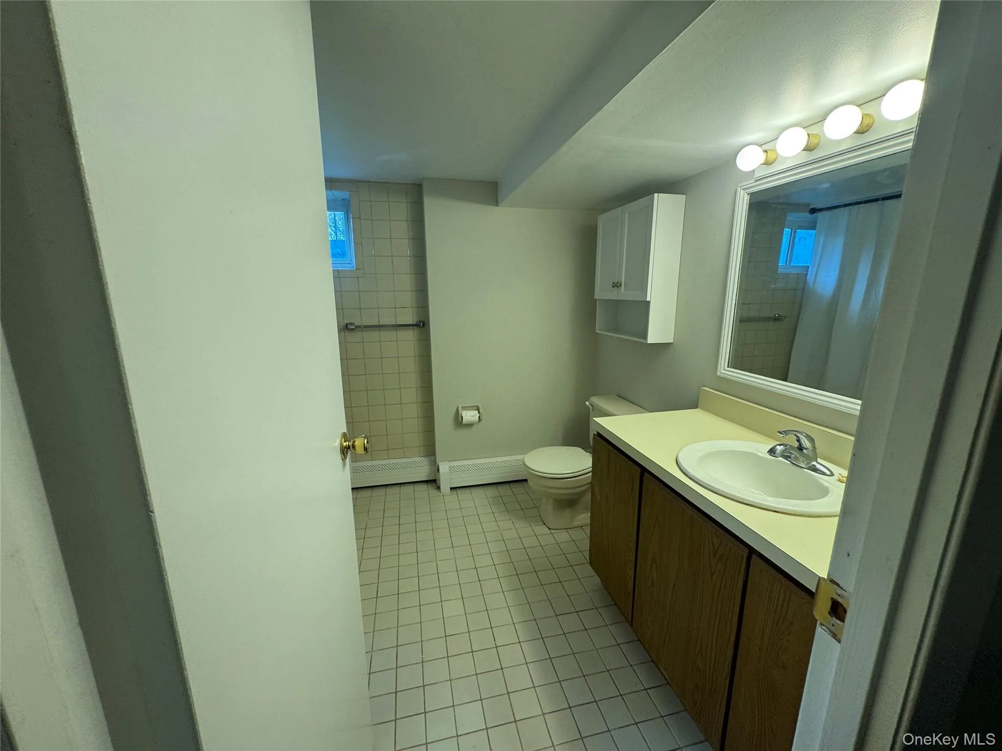 Full bathroom featuring light tile patterned floors, vanity, a shower with shower curtain, and a baseboard radiator Full bathroom featuring light tile patterned floors, vanity, a shower with shower curtain, and a baseboard radiator