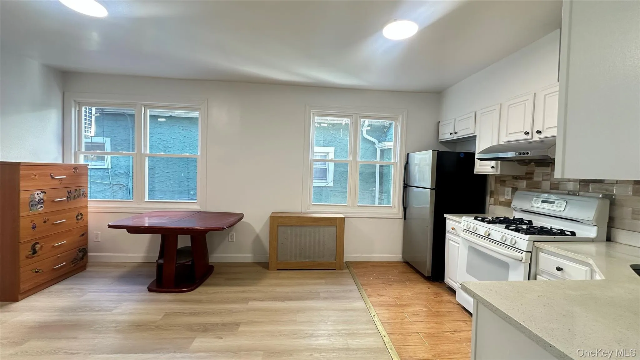 Kitchen featuring white gas stove, light wood-type flooring, white cabinets, decorative backsplash, and under cabinet range hood Kitchen featuring white gas stove, light wood-type flooring, white cabinets, decorative backsplash, and under cabinet range hood