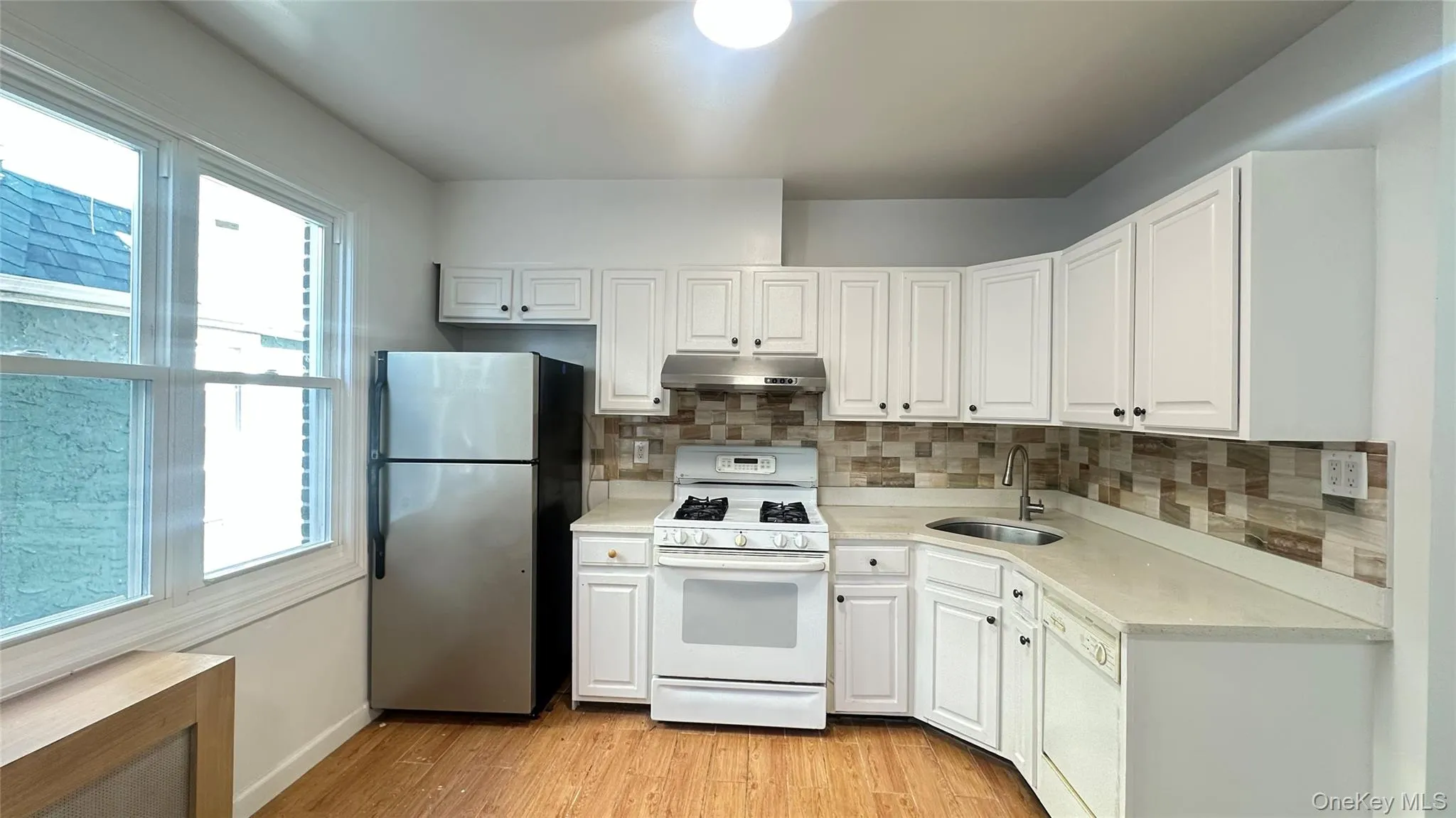Kitchen featuring white appliances, decorative backsplash, white cabinets, light wood-style flooring, and under cabinet range hood Kitchen featuring white appliances, decorative backsplash, white cabinets, light wood-style flooring, and under cabinet range hood