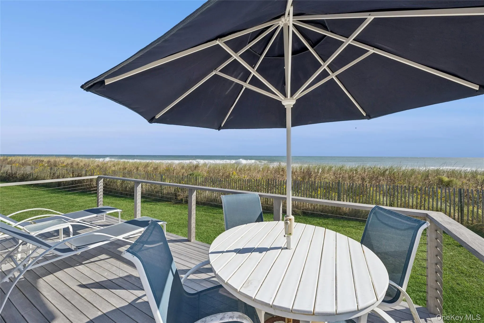 Deck with outdoor dining space, a lawn, and view of water and beach Deck with outdoor dining space, a lawn, and view of water and beach