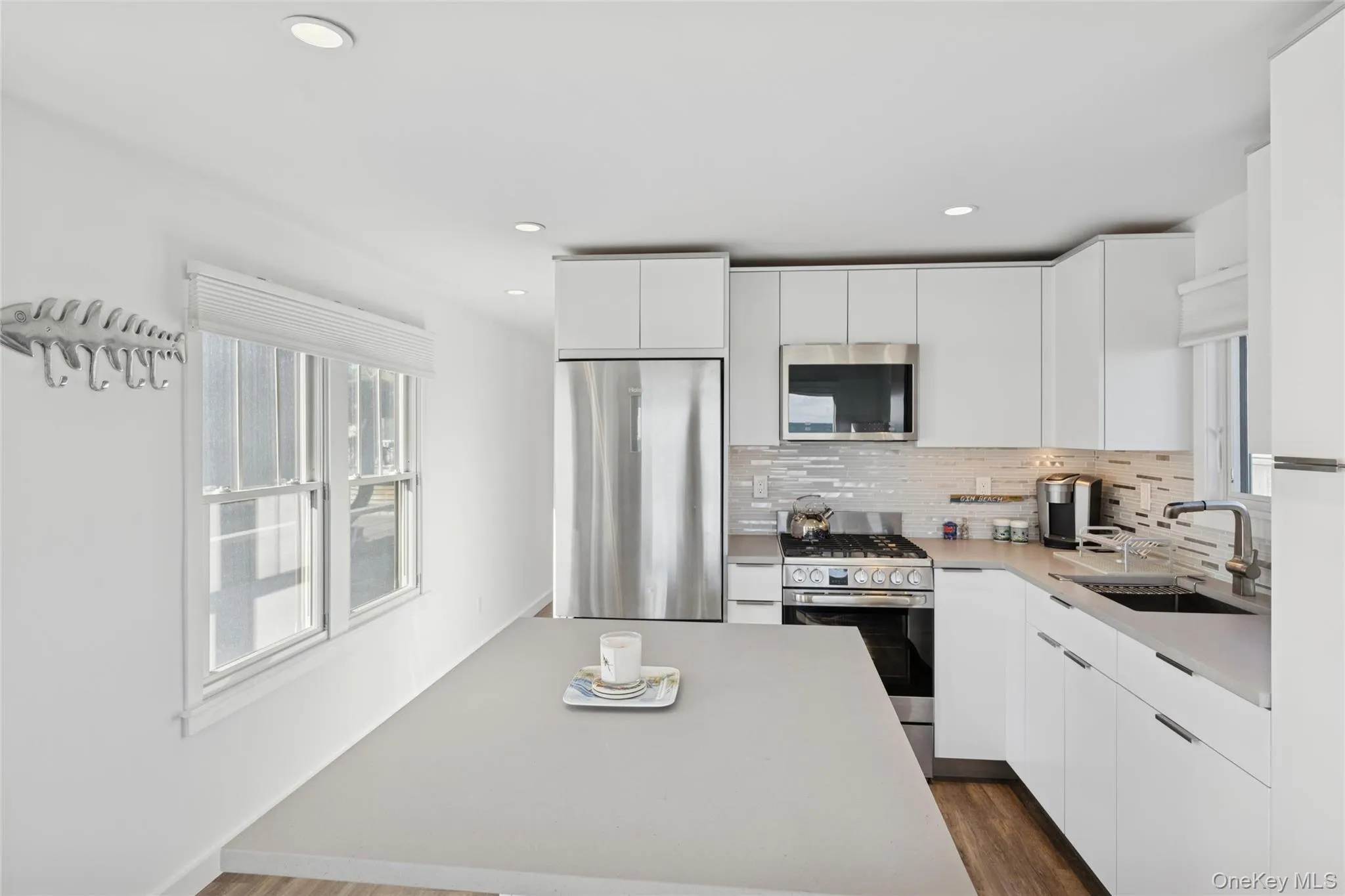 Kitchen with modern cabinets, stainless steel appliances, dark wood finished floors, decorative backsplash, and white cabinetry Kitchen with modern cabinets, stainless steel appliances, dark wood finished floors, decorative backsplash, and white cabinetry