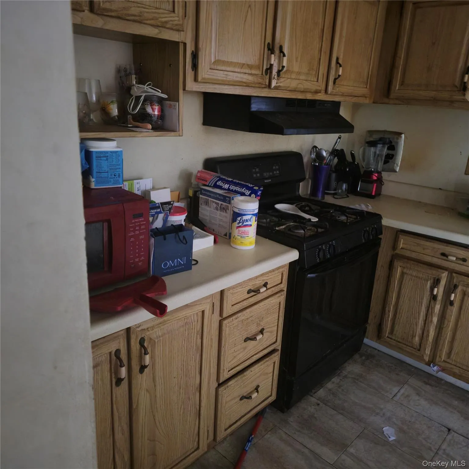 Kitchen with black range with gas cooktop, light countertops, exhaust hood, and brown cabinetry Kitchen with black range with gas cooktop, light countertops, exhaust hood, and brown cabinetry