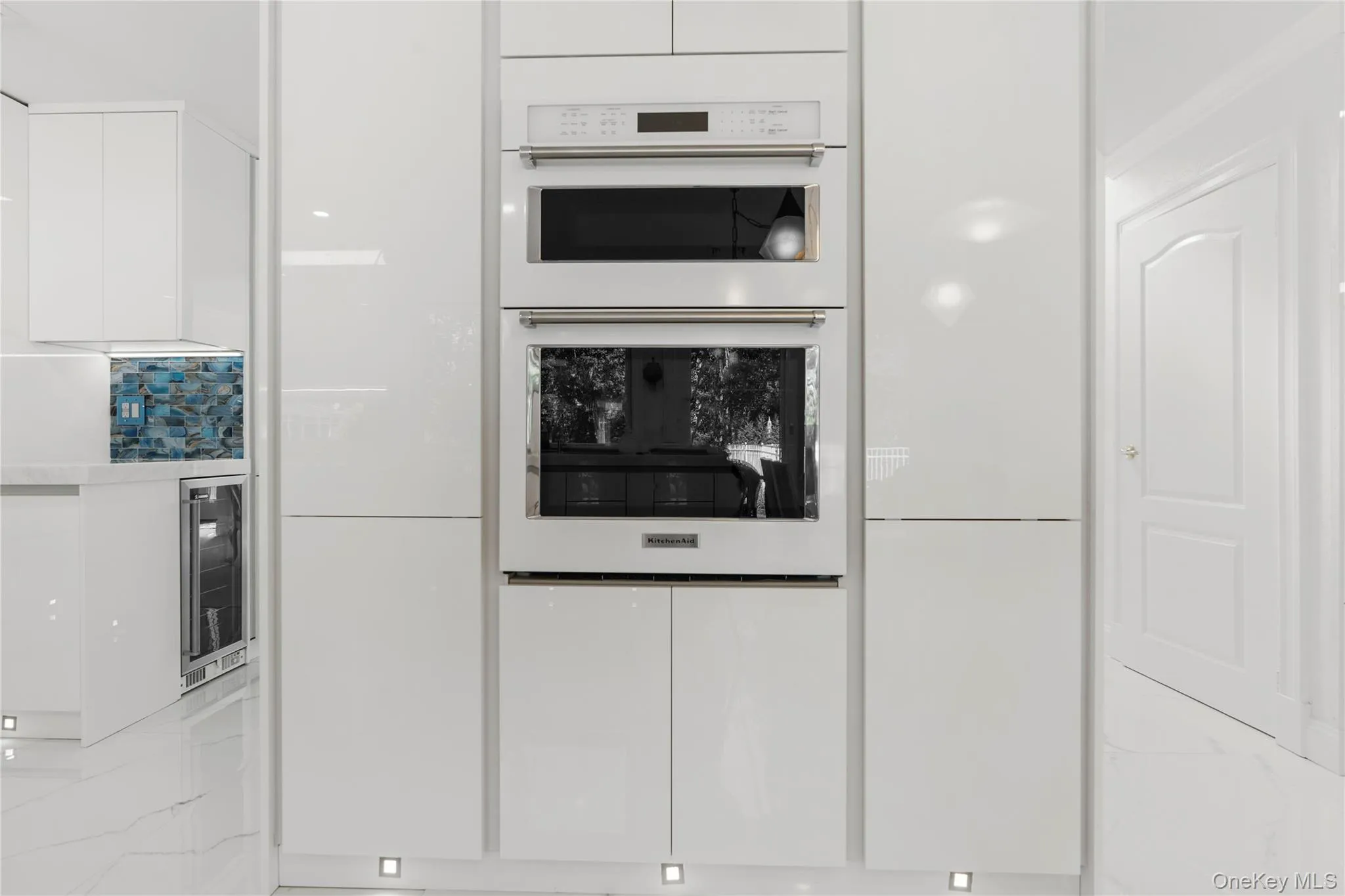 Kitchen with white cabinets, double oven, modern cabinets, beverage cooler, and light marble finish flooring Kitchen with white cabinets, double oven, modern cabinets, beverage cooler, and light marble finish flooring