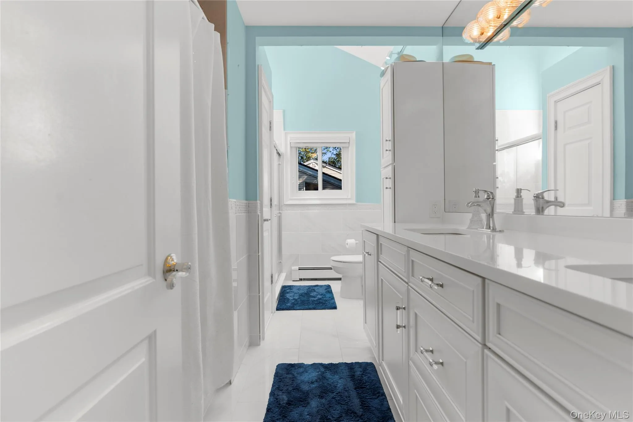 Full bathroom with double vanity, a shower with curtain, tile walls and light tile patterned floors. Full bathroom with double vanity, a shower with curtain, tile walls and light tile patterned floors.