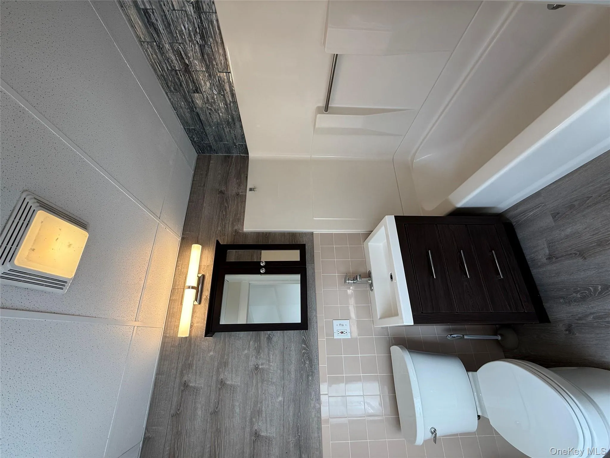 Bathroom with tile walls, dark wood-style flooring, vanity, tub / shower combination, and a drop ceiling Bathroom with tile walls, dark wood-style flooring, vanity, tub / shower combination, and a drop ceiling