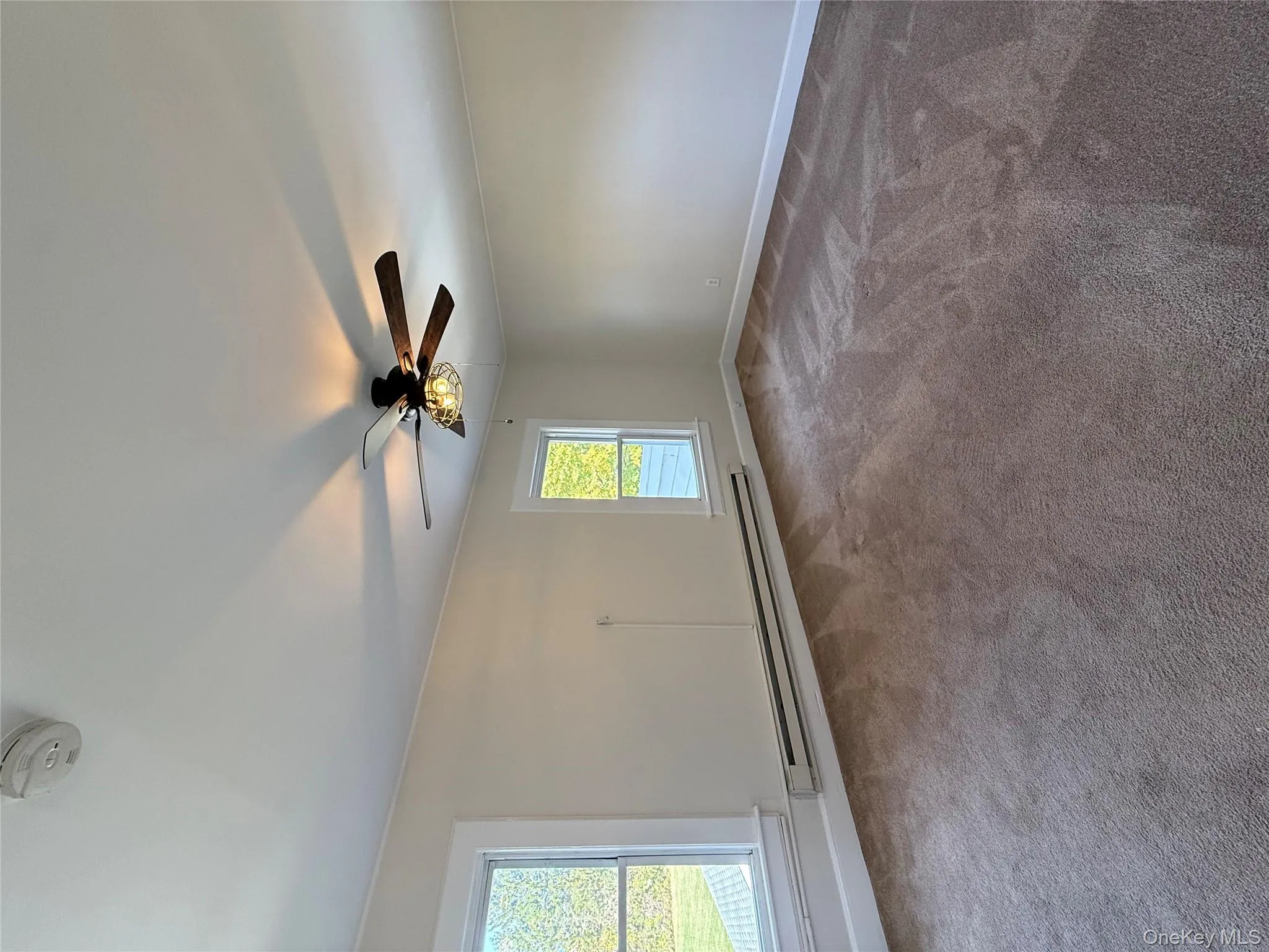 Carpeted empty room with baseboard heating, a smoke detector, and ceiling fan Carpeted empty room with baseboard heating, a smoke detector, and ceiling fan