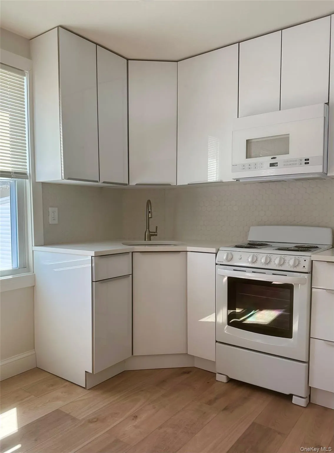 Kitchen with white appliances, white cabinetry, backsplash, and light wood-type flooring Kitchen with white appliances, white cabinetry, backsplash, and light wood-type flooring