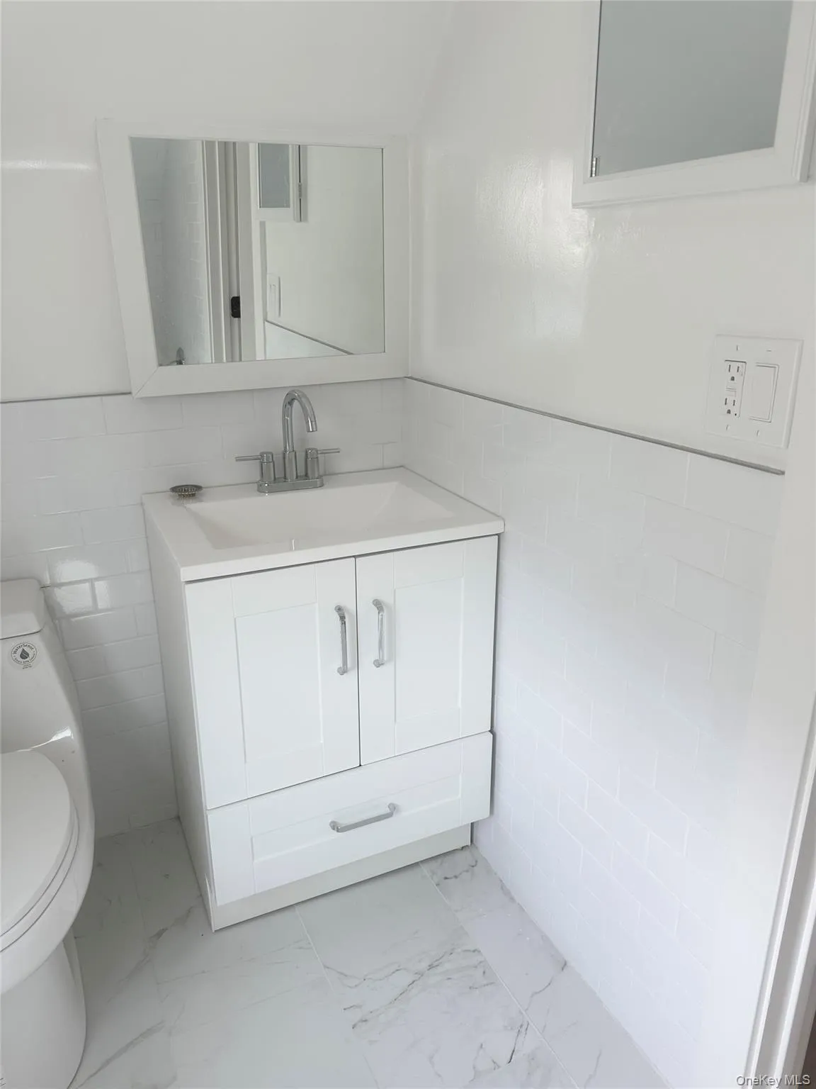 Bathroom with tile walls, vanity, light marble finish flooring, and a wainscoted wall Bathroom with tile walls, vanity, light marble finish flooring, and a wainscoted wall