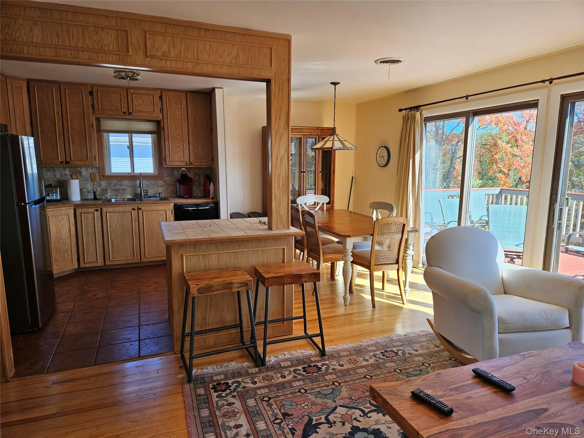 Kitchen with freestanding refrigerator, tile counters, tasteful backsplash, hanging light fixtures, and dark wood-style floors Kitchen with freestanding refrigerator, tile counters, tasteful backsplash, hanging light fixtures, and dark wood-style floors