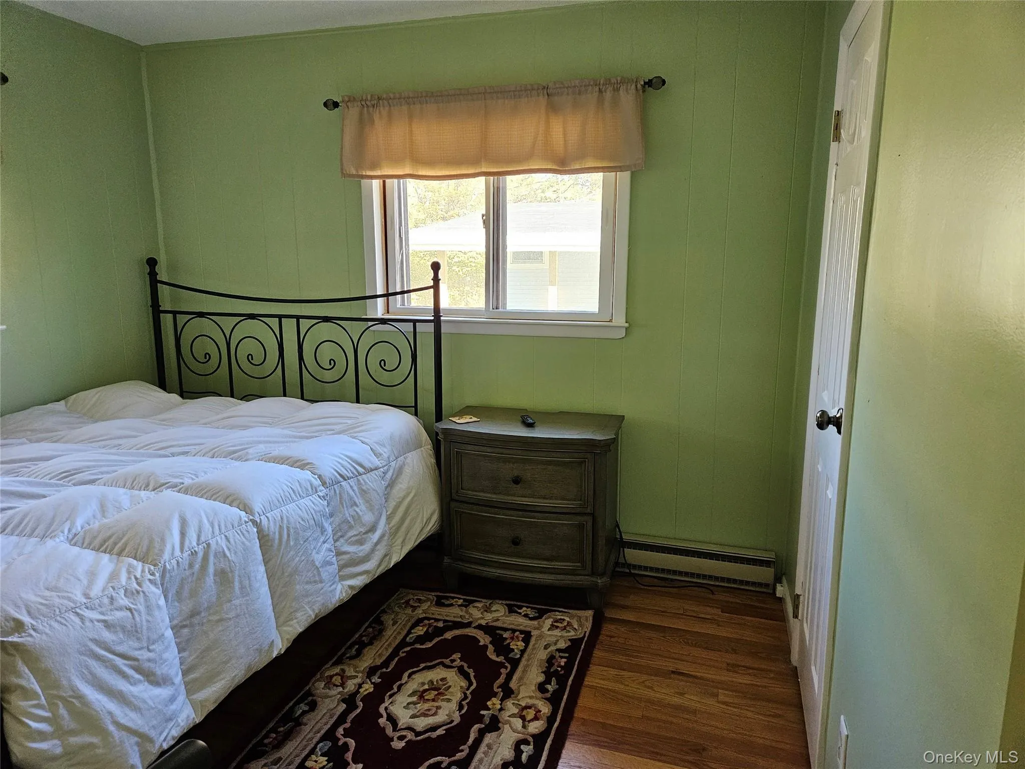 Bedroom featuring dark wood-style flooring and a baseboard heating unit Bedroom featuring dark wood-style flooring and a baseboard heating unit