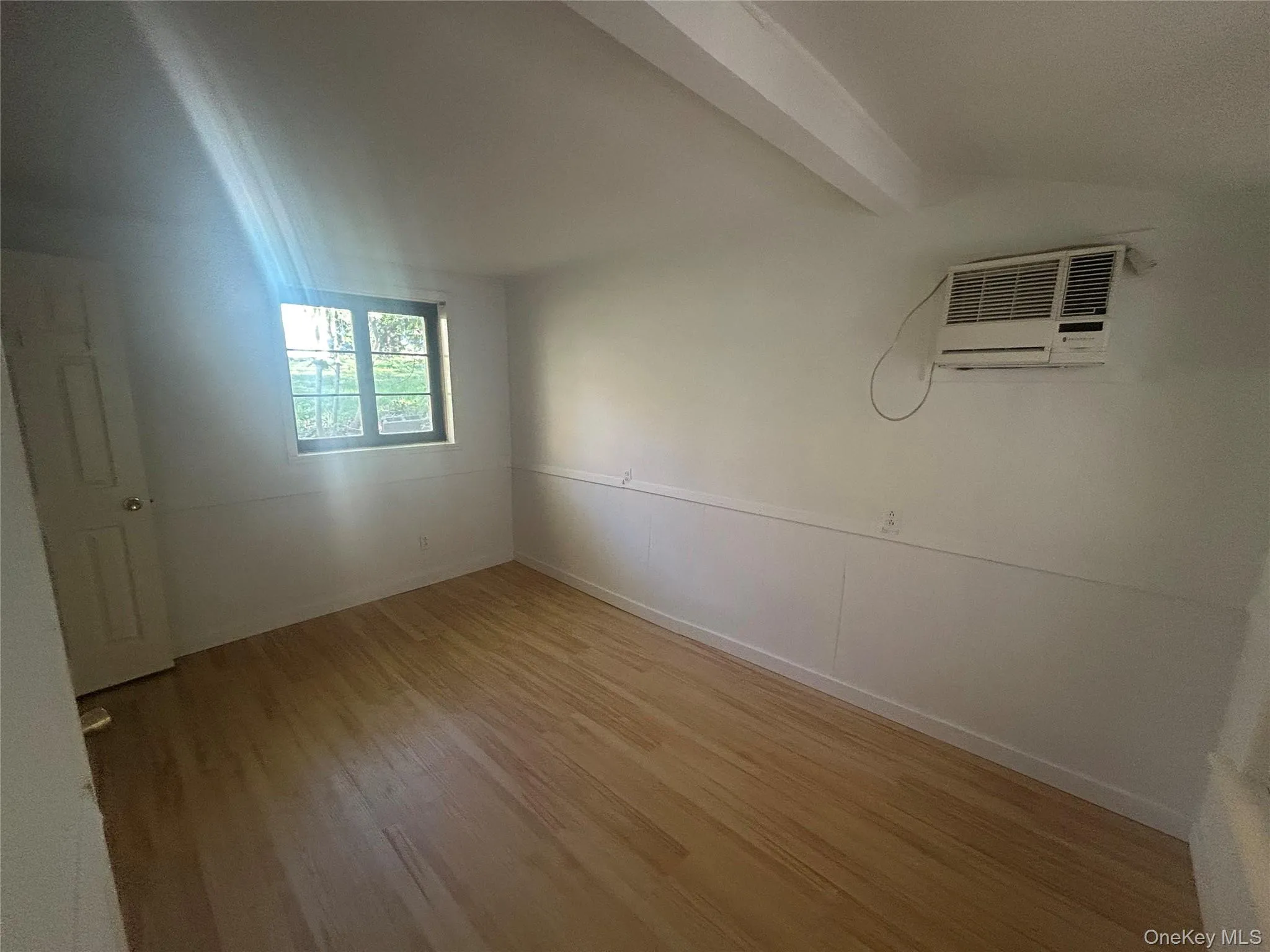 Unfurnished room featuring light wood finished floors and a wall mounted air conditioner Unfurnished room featuring light wood finished floors and a wall mounted air conditioner