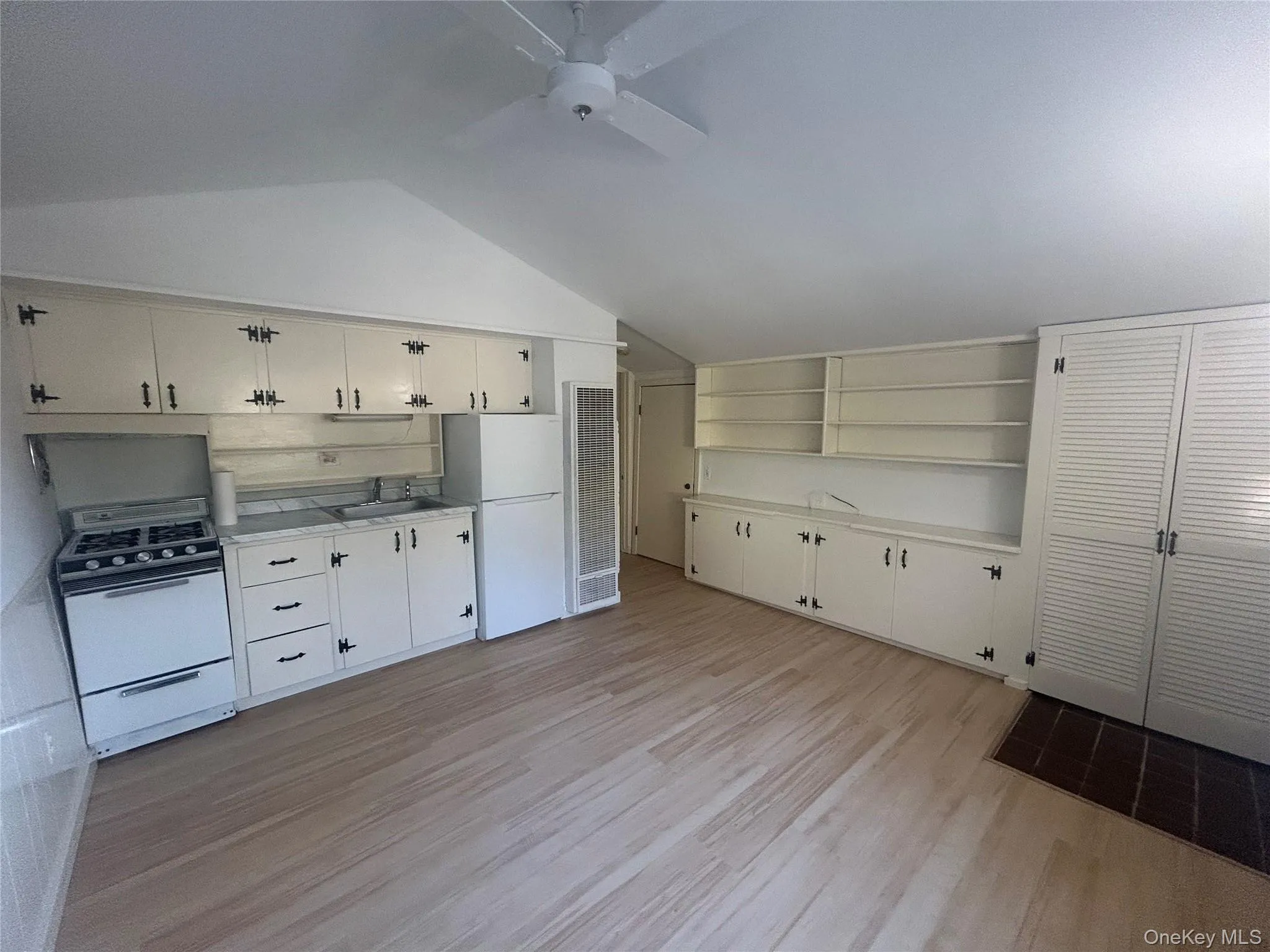 Kitchen featuring white appliances, light wood-style flooring, light countertops, vaulted ceiling, and a heating unit Kitchen featuring white appliances, light wood-style flooring, light countertops, vaulted ceiling, and a heating unit