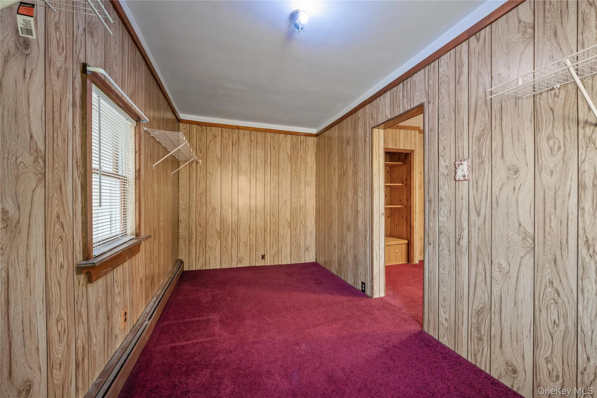 Spare room featuring a baseboard heating unit, wooden walls, dark carpet, and crown molding Spare room featuring a baseboard heating unit, wooden walls, dark carpet, and crown molding