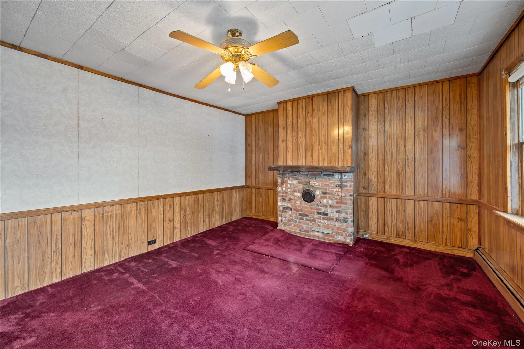 Unfurnished living room featuring wooden walls, crown molding, dark carpet, a baseboard heating unit, and a ceiling fan Unfurnished living room featuring wooden walls, crown molding, dark carpet, a baseboard heating unit, and a ceiling fan
