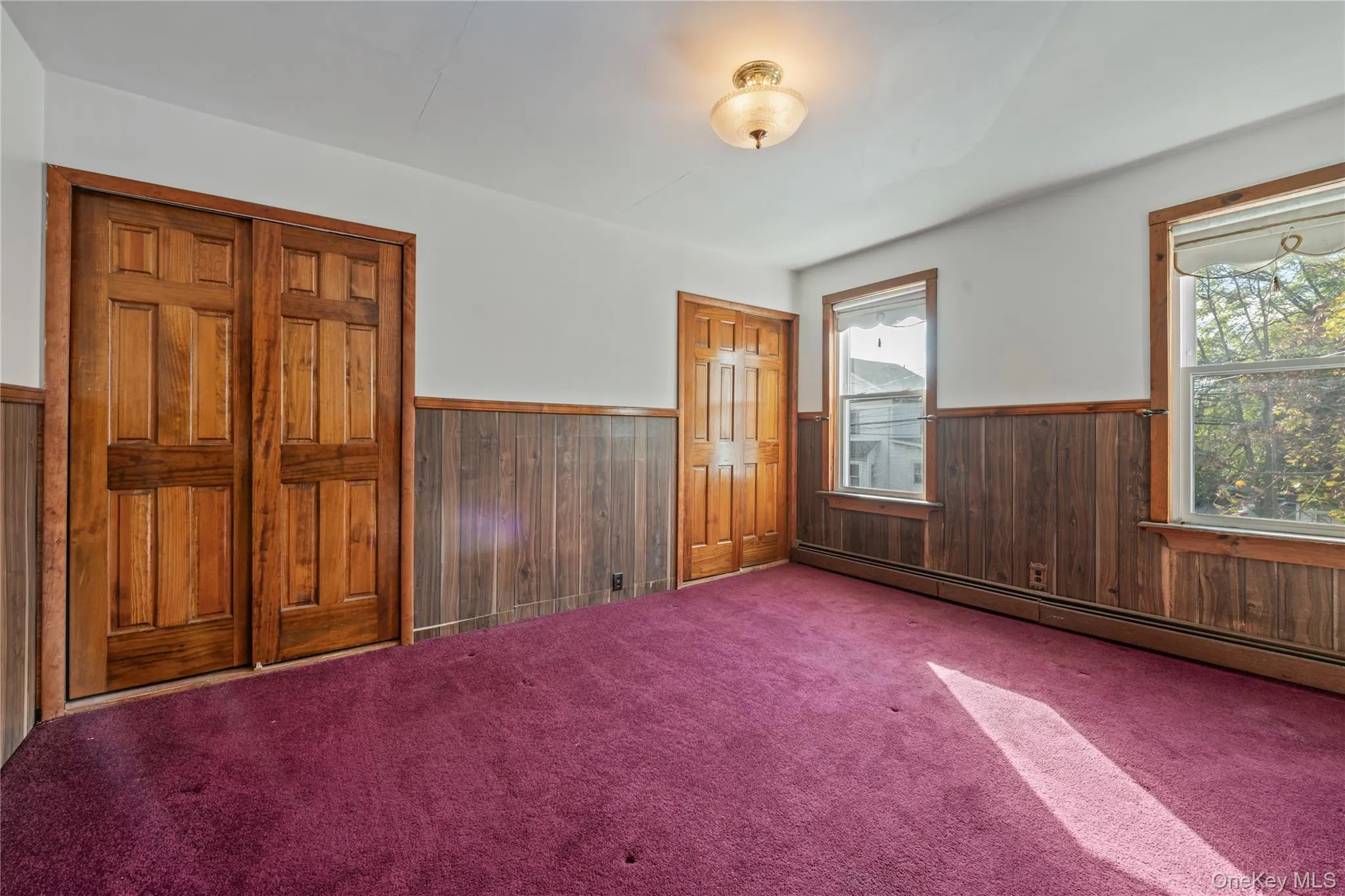 Carpeted spare room with wood walls, wainscoting, and baseboard heating Carpeted spare room with wood walls, wainscoting, and baseboard heating