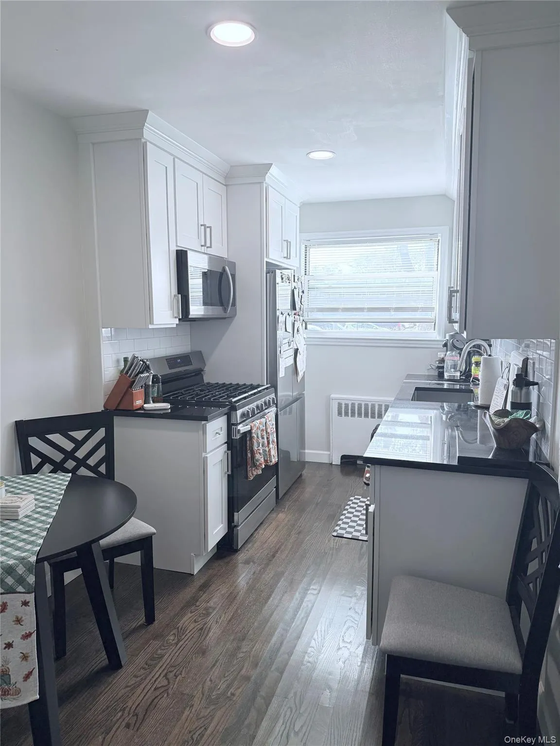 Kitchen featuring appliances with stainless steel finishes, tasteful backsplash, dark countertops, dark wood-type flooring, and white cabinets Kitchen featuring appliances with stainless steel finishes, tasteful backsplash, dark countertops, dark wood-type flooring, and white cabinets