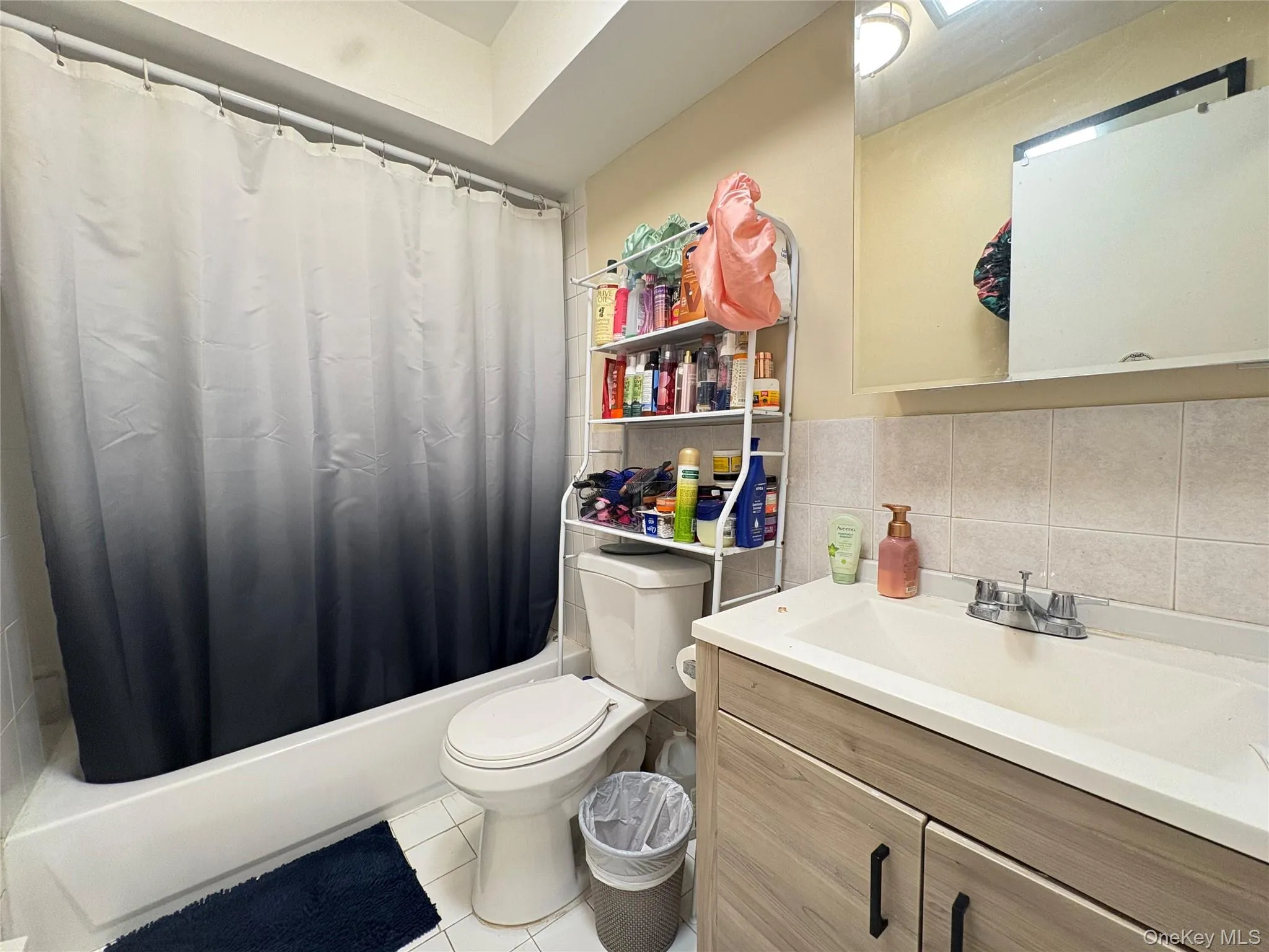 Full bathroom featuring tile walls, shower / tub combo with curtain, tile patterned floors, vanity, and backsplash Full bathroom featuring tile walls, shower / tub combo with curtain, tile patterned floors, vanity, and backsplash