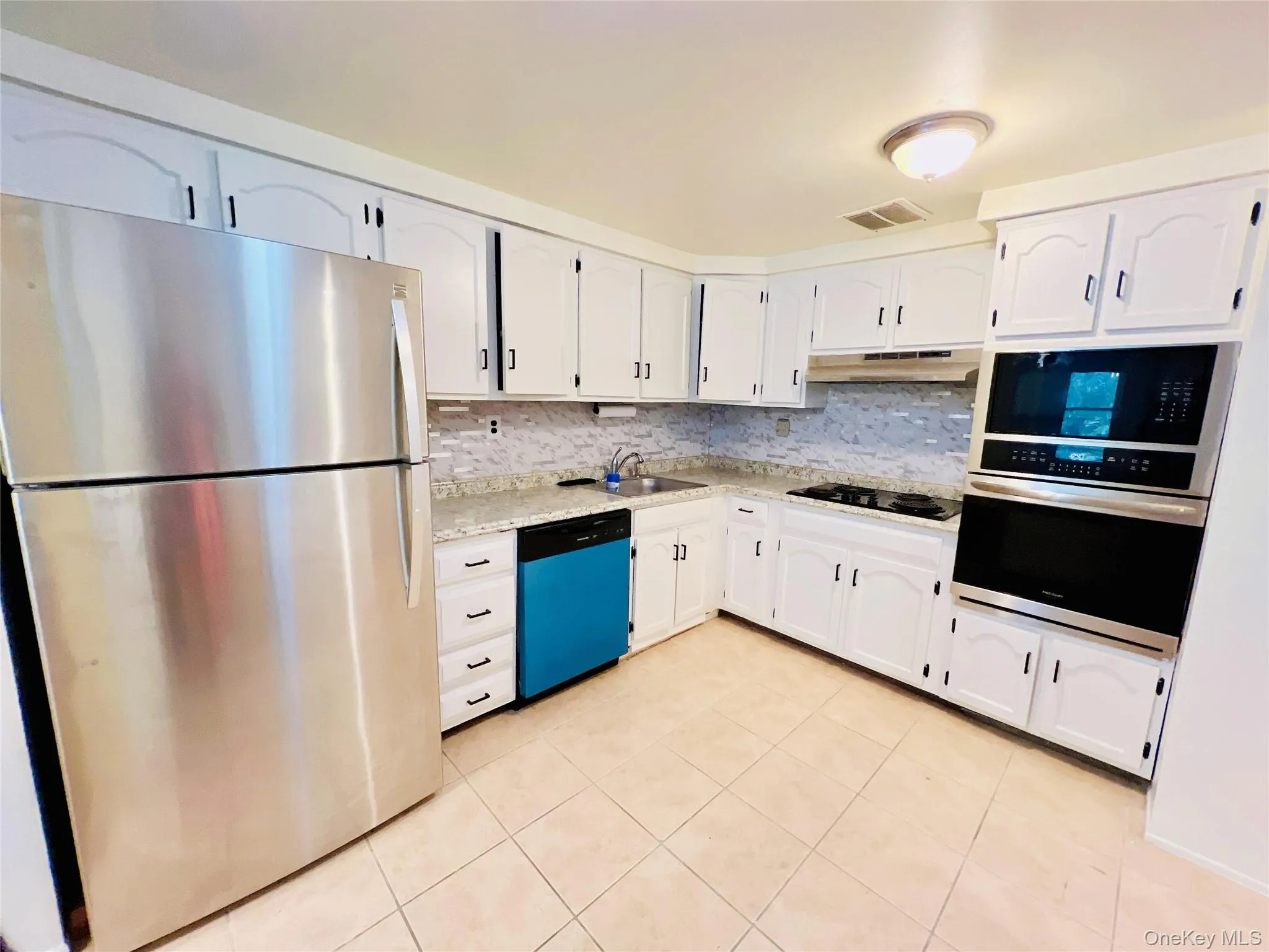 Kitchen featuring appliances with stainless steel finishes, backsplash, light tile patterned flooring, and white cabinets Kitchen featuring appliances with stainless steel finishes, backsplash, light tile patterned flooring, and white cabinets