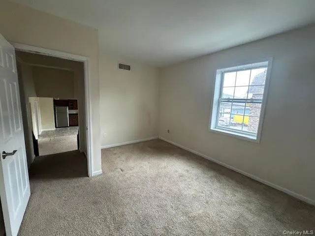Unfurnished bedroom with light carpet and stainless steel fridge Unfurnished bedroom with light carpet and stainless steel fridge