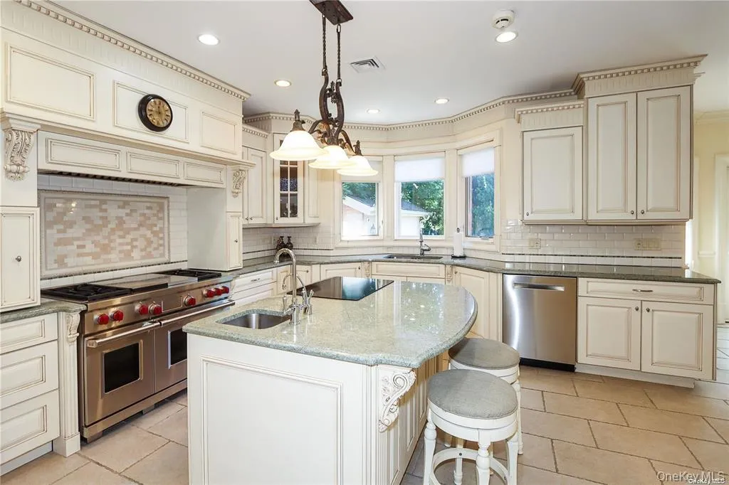 Kitchen with cream cabinetry, dark stone counters, backsplash, stainless steel appliances, and recessed lighting Kitchen with cream cabinetry, dark stone counters, backsplash, stainless steel appliances, and recessed lighting