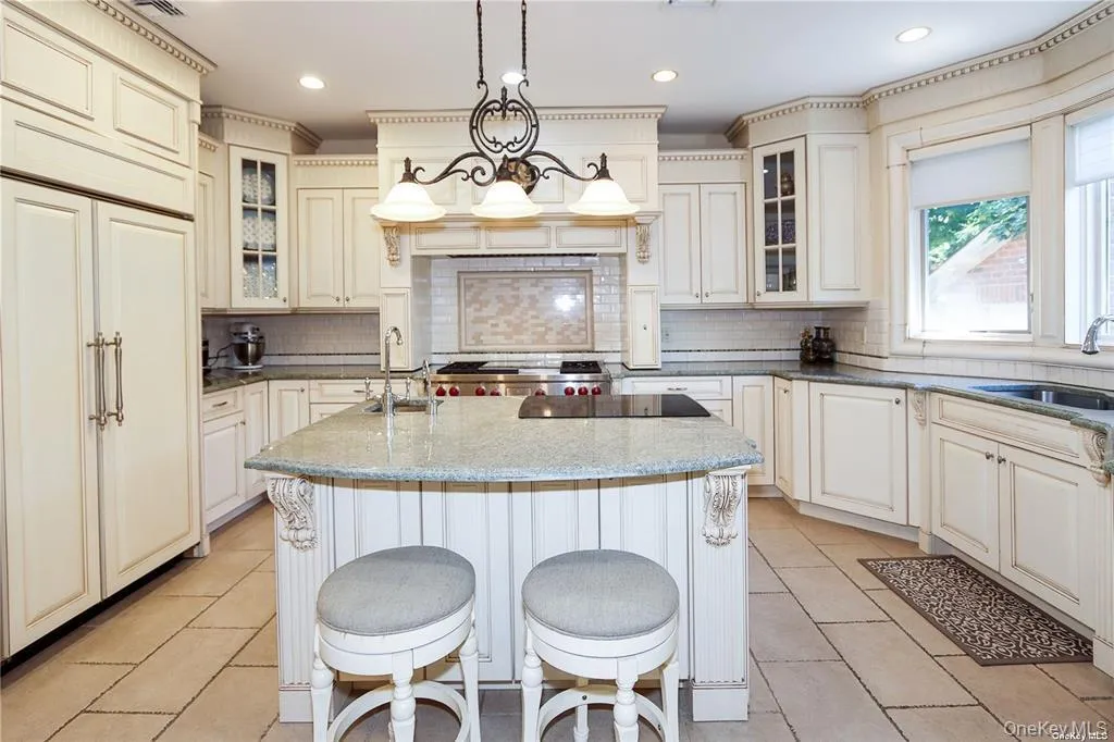 Kitchen featuring glass insert cabinets, a center island with sink, dark stone counters, hanging light fixtures, and decorative backsplash Kitchen featuring glass insert cabinets, a center island with sink, dark stone counters, hanging light fixtures, and decorative backsplash