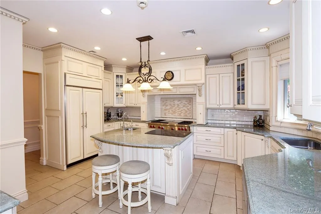 Kitchen with dark stone counters, a kitchen island with sink, hanging light fixtures, a breakfast bar, and glass insert cabinets Kitchen with dark stone counters, a kitchen island with sink, hanging light fixtures, a breakfast bar, and glass insert cabinets