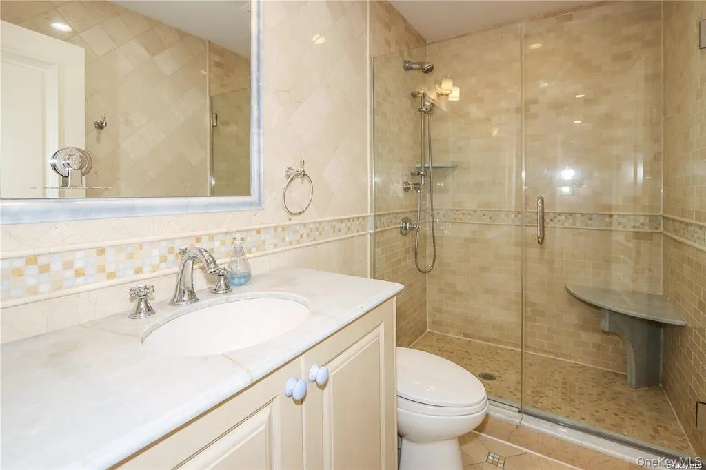 Full bath with tile walls, a shower stall, vanity, light tile patterned floors, and backsplash Full bath with tile walls, a shower stall, vanity, light tile patterned floors, and backsplash