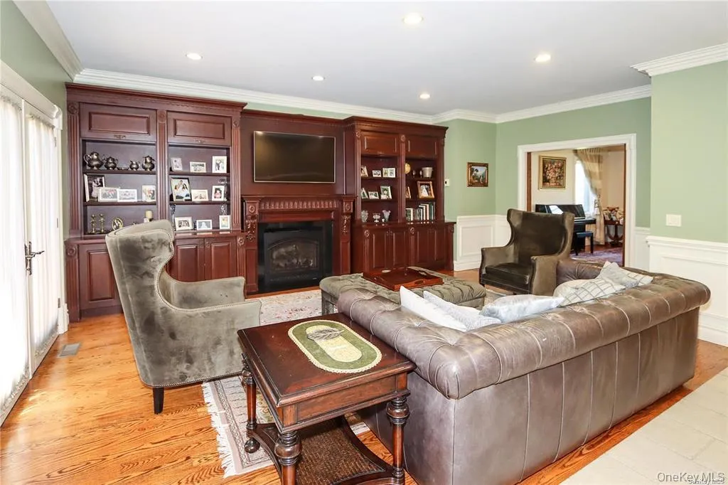Living room with a fireplace, ornamental molding, recessed lighting, light wood-style flooring, and wainscoting Living room with a fireplace, ornamental molding, recessed lighting, light wood-style flooring, and wainscoting