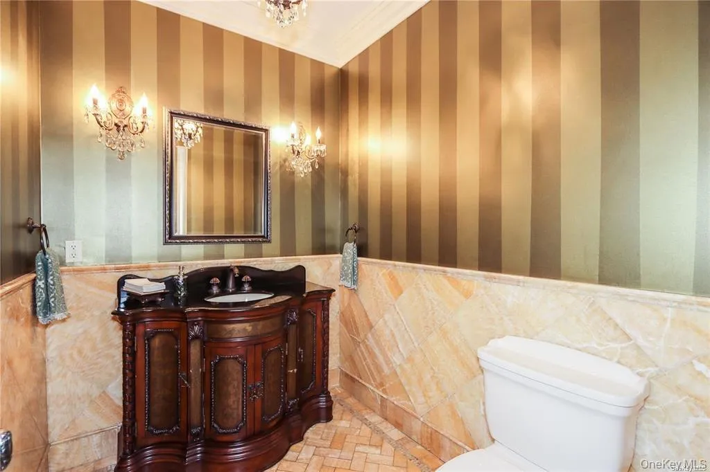 Half bathroom featuring crown molding, vanity, wainscoting, tile walls, and wallpapered walls Half bathroom featuring crown molding, vanity, wainscoting, tile walls, and wallpapered walls
