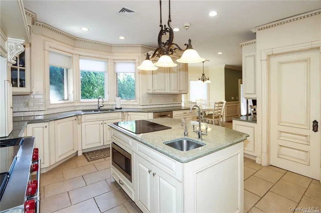 Kitchen featuring appliances with stainless steel finishes, hanging light fixtures, dark stone countertops, a kitchen island with sink, and decorative backsplash Kitchen featuring appliances with stainless steel finishes, hanging light fixtures, dark stone countertops, a kitchen island with sink, and decorative backsplash