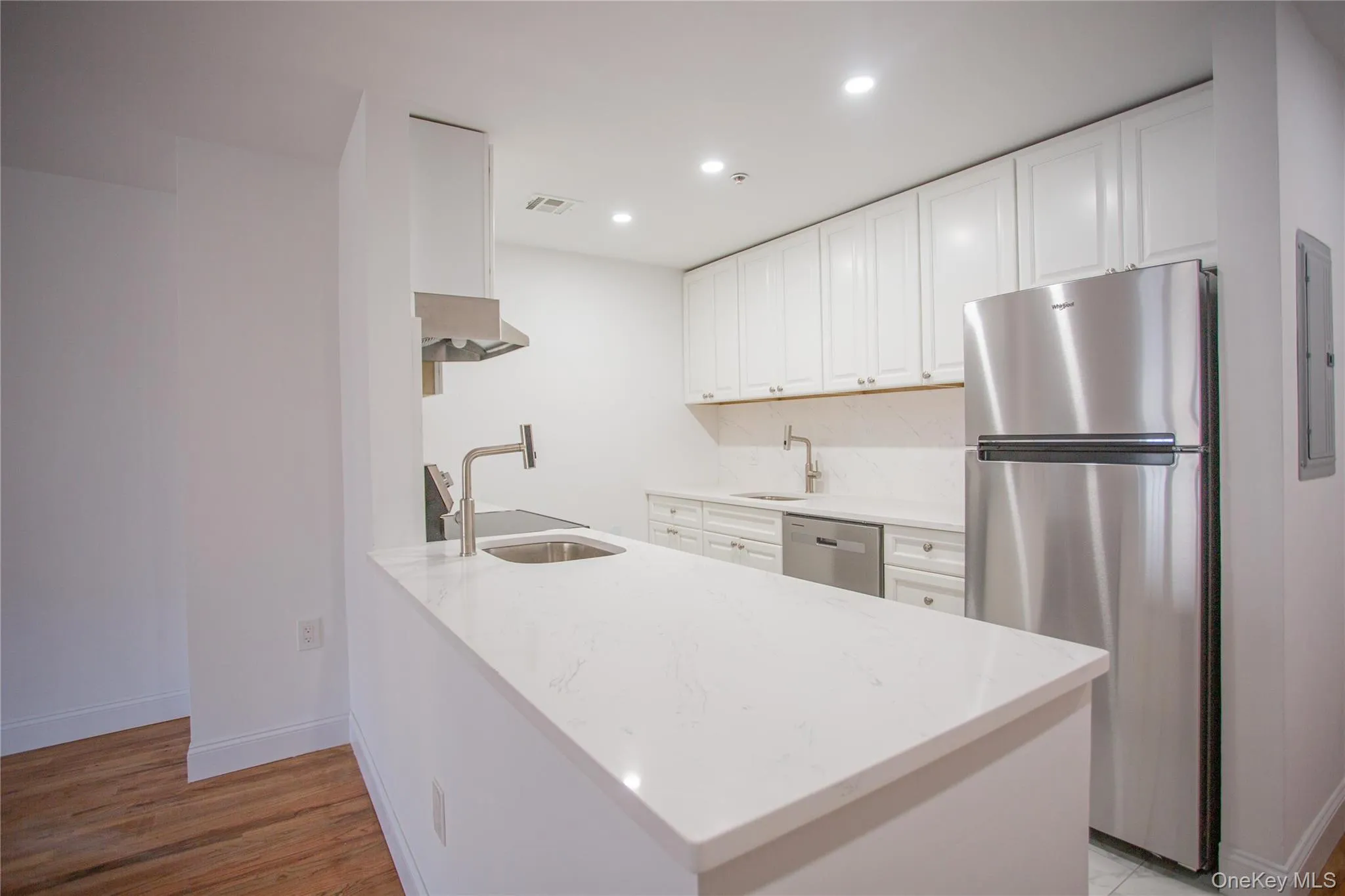 Kitchen with light stone counters, appliances with stainless steel finishes, white cabinets, recessed lighting, and a peninsula Kitchen with light stone counters, appliances with stainless steel finishes, white cabinets, recessed lighting, and a peninsula