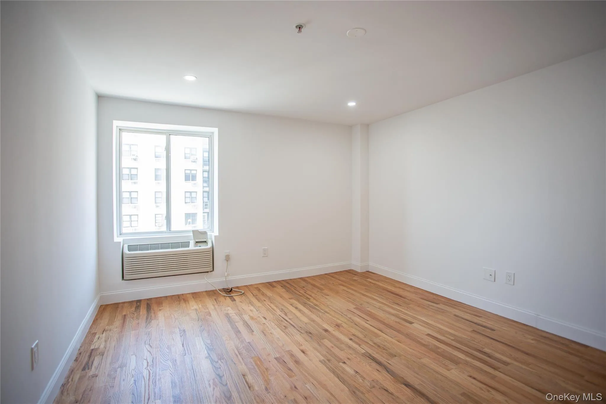 Empty room with light wood-style floors, recessed lighting, and an AC wall unit Empty room with light wood-style floors, recessed lighting, and an AC wall unit