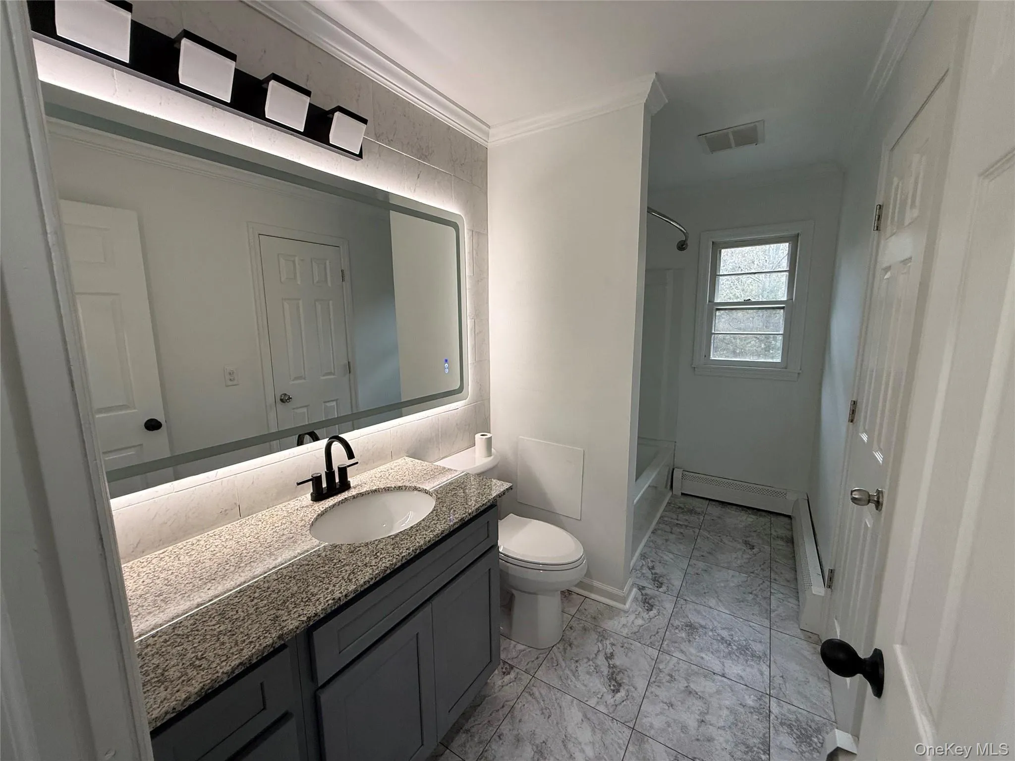 Bathroom featuring ornamental molding, vanity, shower / bathtub combination, and a baseboard heating unit Bathroom featuring ornamental molding, vanity, shower / bathtub combination, and a baseboard heating unit