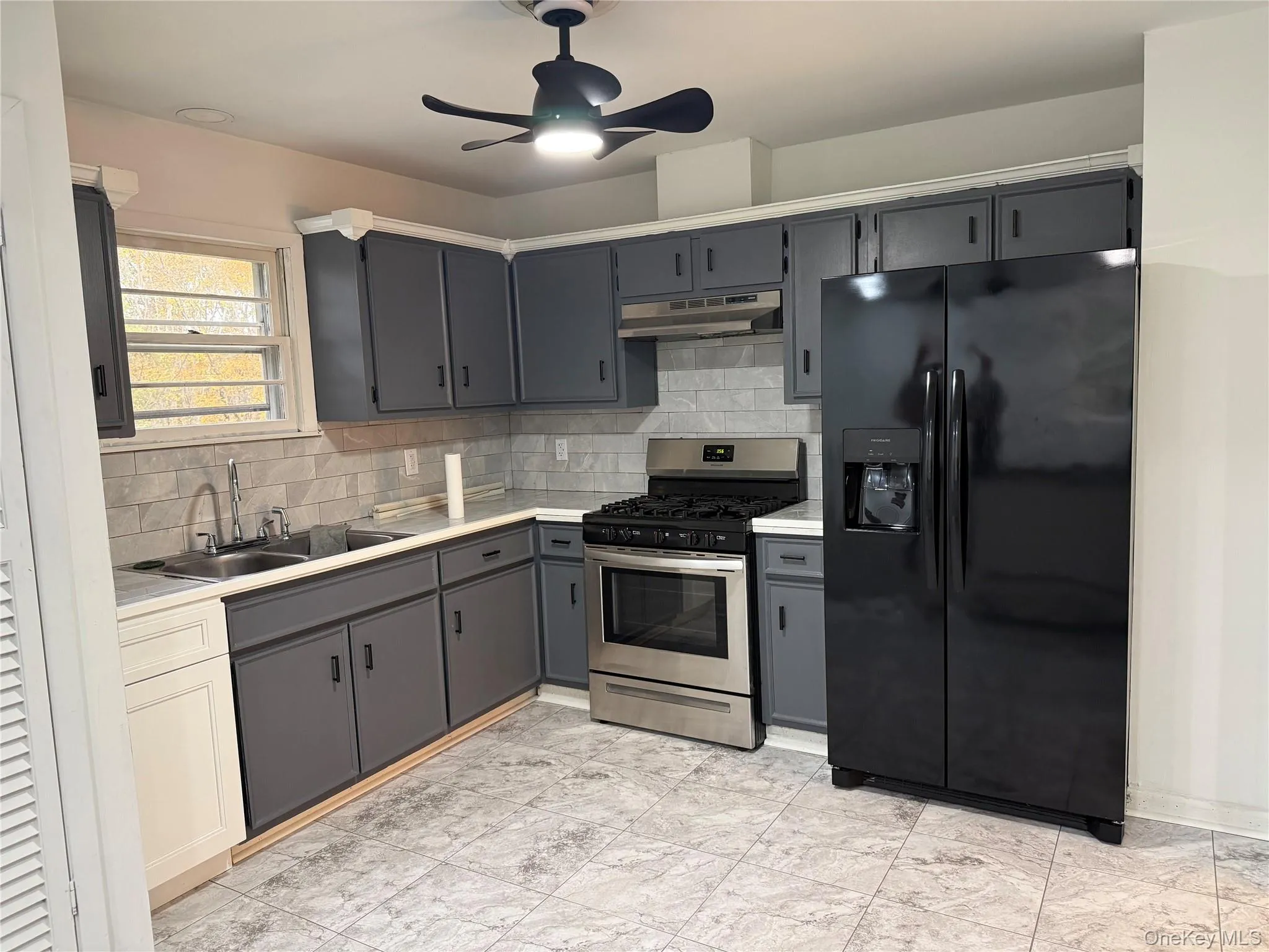 Kitchen with gray cabinetry, black fridge with ice dispenser, tasteful backsplash, and stainless steel range with gas stovetop Kitchen with gray cabinetry, black fridge with ice dispenser, tasteful backsplash, and stainless steel range with gas stovetop