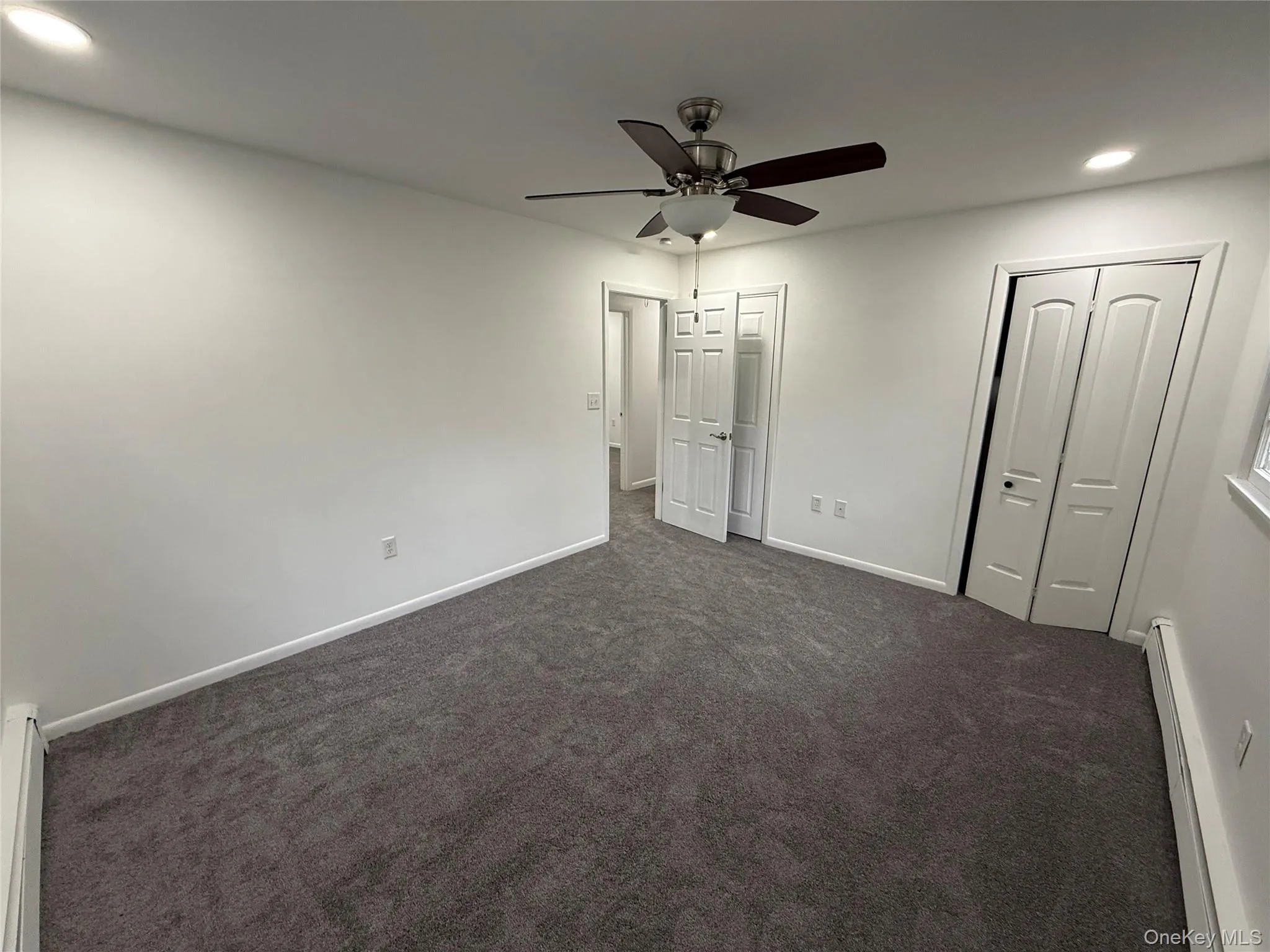 Unfurnished bedroom with recessed lighting, a baseboard radiator, dark colored carpet, a ceiling fan, and a baseboard heating unit Unfurnished bedroom with recessed lighting, a baseboard radiator, dark colored carpet, a ceiling fan, and a baseboard heating unit